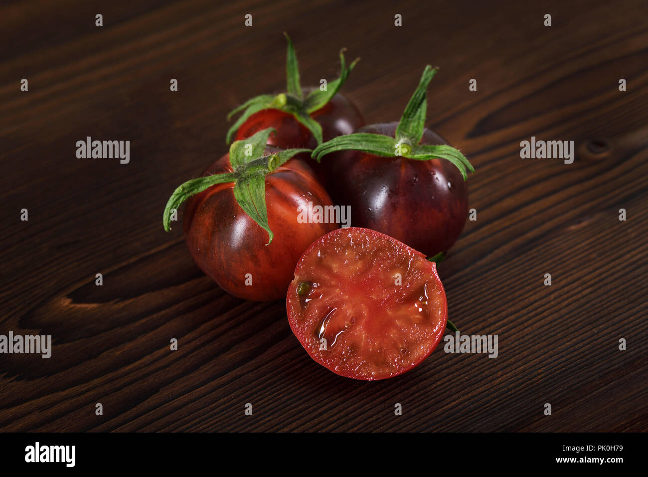 Indigo Rose Bio Tomaten mit tief-roten Farbe aus und reichen Geschmack, anti-Krebs, die reich an Antioxidantien und Anthocyane. Künstlerische noch Leben auf der dunklen Woo Stockfoto