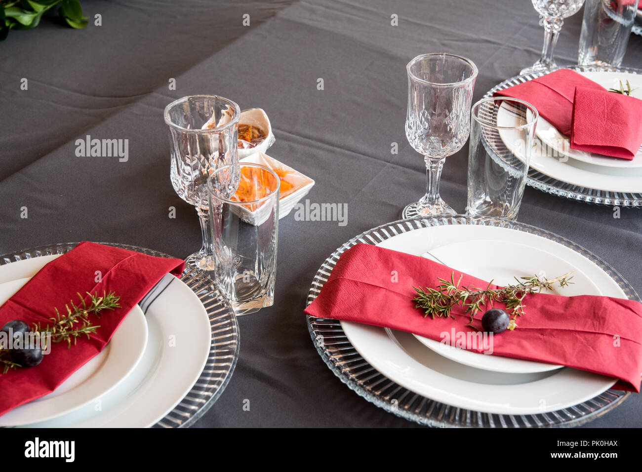 Ein Mittagstisch mit unter Teller Set, schöne graue und weiße Platten, rot Serviette, kleine dekorative tree branch, zwei Trauben mit Blumen und Obst Dekor Stockfoto