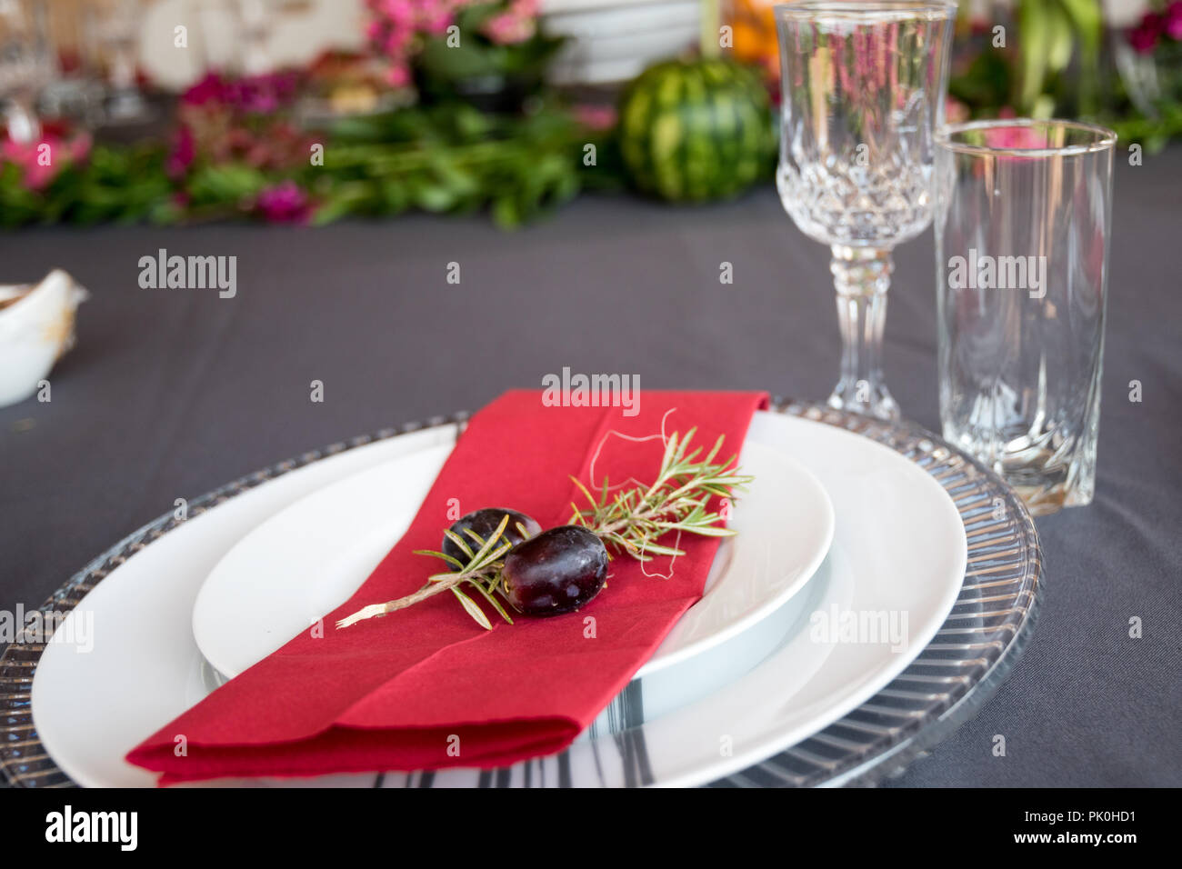 Ein Mittagstisch mit unter Teller Set, schöne graue und weiße Platten, rot Serviette, kleine dekorative tree branch, zwei Trauben mit Blumen und Obst Dekor. Stockfoto
