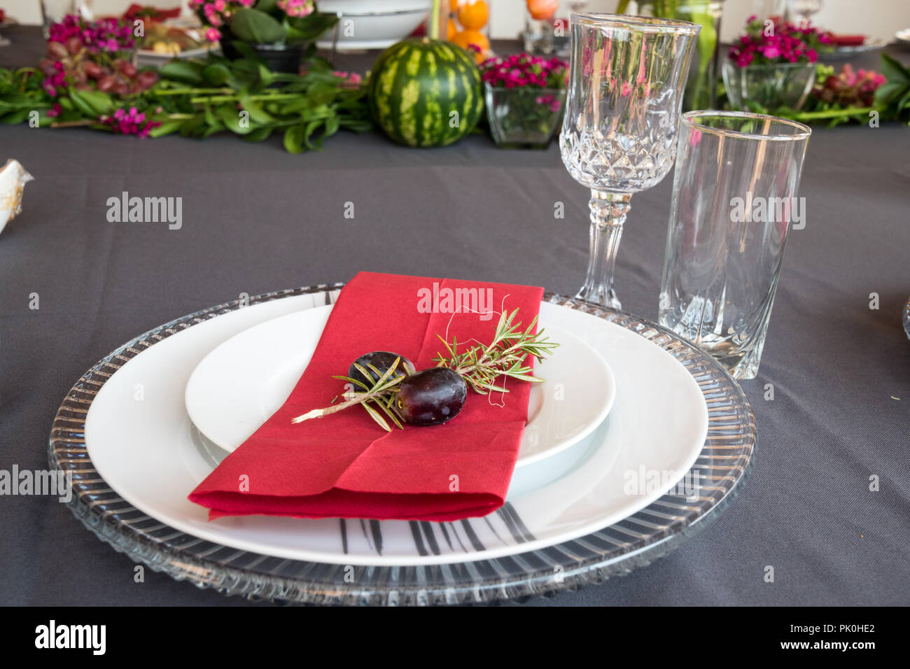 Ein Mittagstisch mit unter Teller Set, schöne graue und weiße Platten, rot Serviette, kleine dekorative tree branch, zwei Trauben mit Blumen und Obst Dekor. Stockfoto