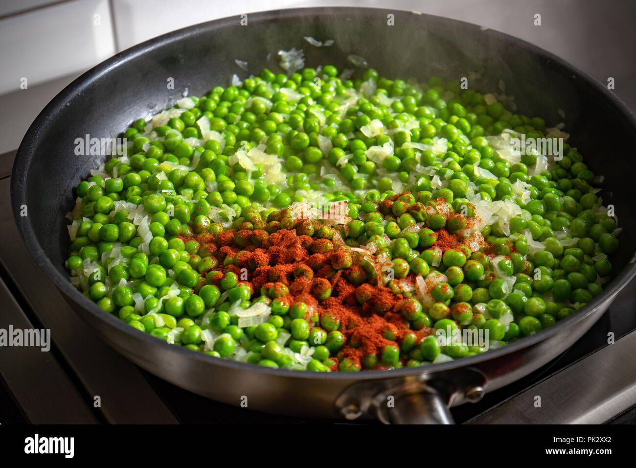 Gehackte Zwiebel und Paprikapulver, grüne Erbsen in die Pfanne hinzugefügt Stockfoto