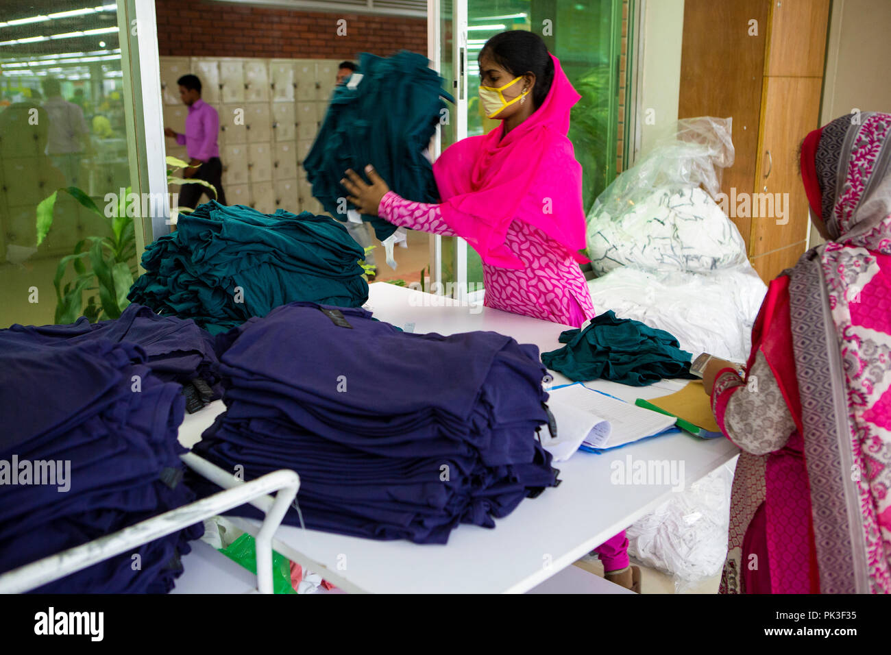 Eine Näherin sortiert durch Stapel von Kleidung in einer Textilfabrik in Bangladesch. Stockfoto