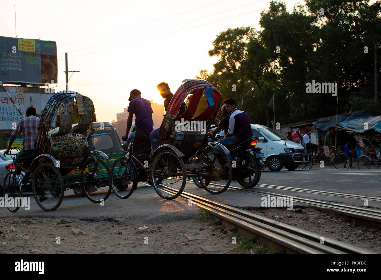 Autos und Rikschas Überquerung der Bahnlinie wie die Sonne in Dhaka, Bangladesh. Stockfoto