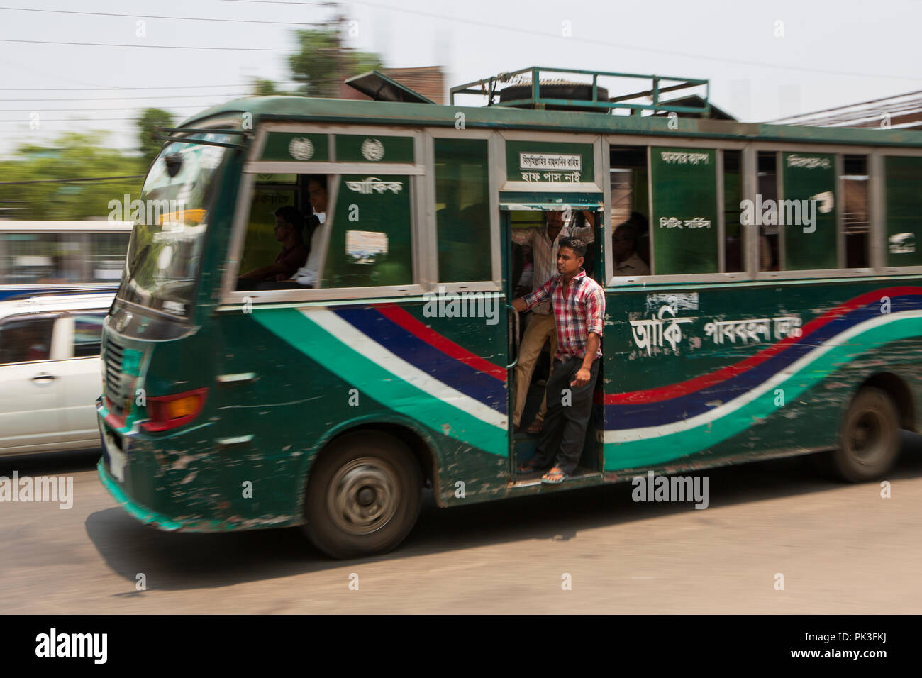 Ein Mann hängt an der offenen Tür von einem Bus auf den Straßen von Dhaka, Bangladesch. Stockfoto