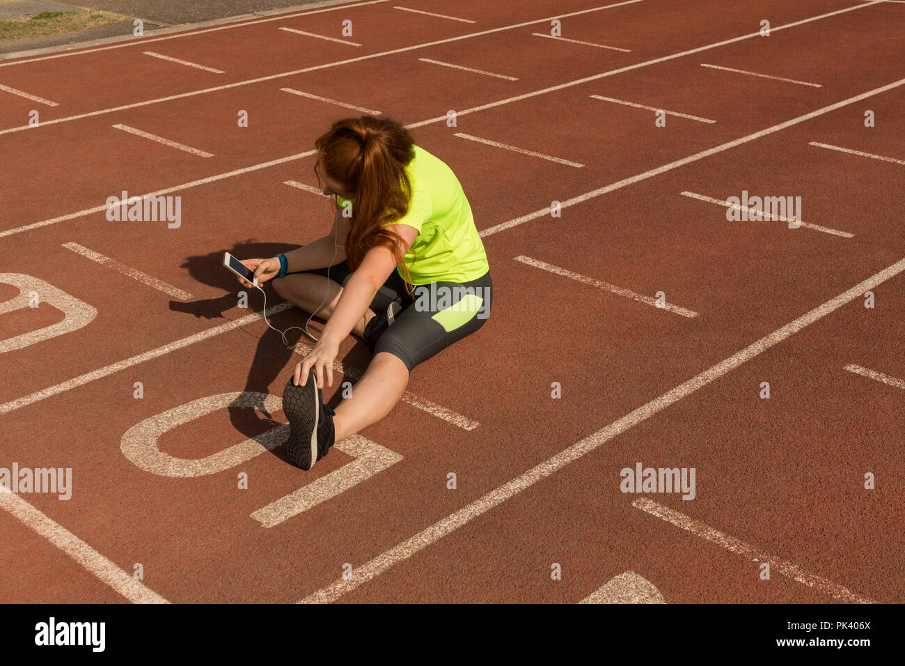 Weibliche athletische mit Handy während des Trainings auf der Laufstrecke Stockfoto