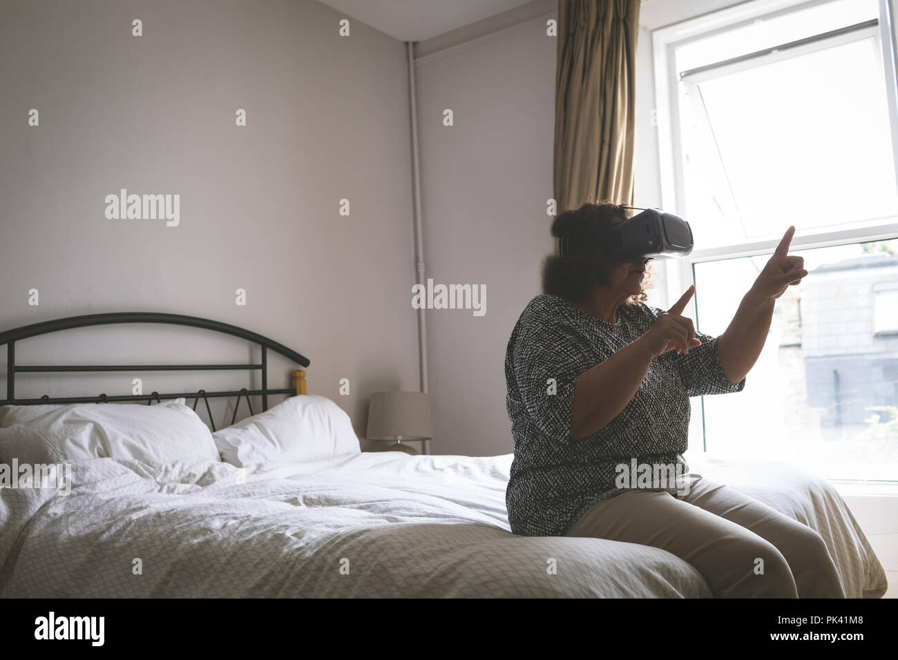 Ältere Frau mit Virtual reality Headset im Schlafzimmer Stockfoto