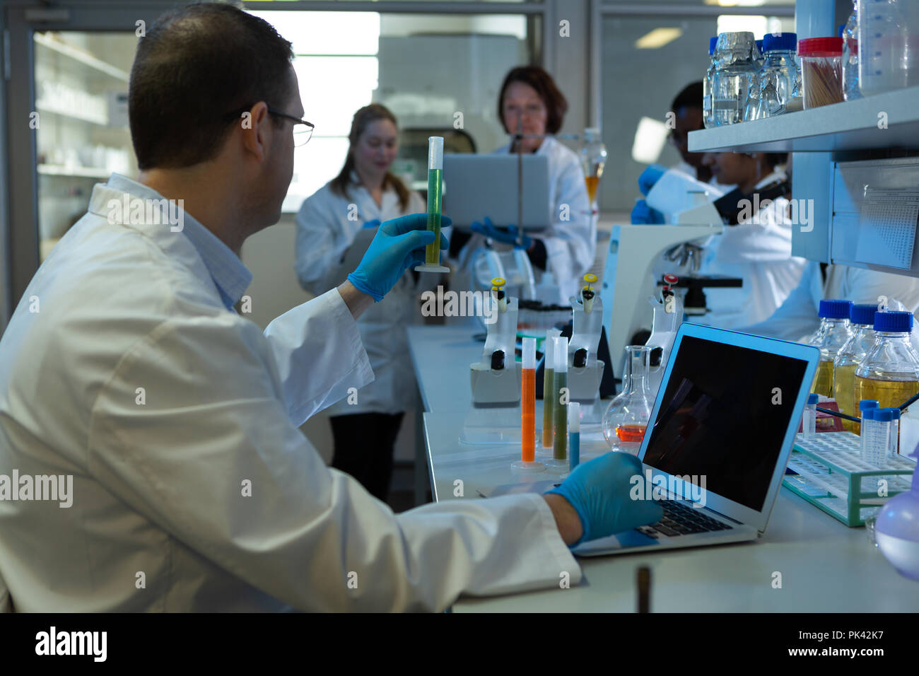 Männliche Wissenschaftler mit Laptop halten Reagenzglas Stockfoto