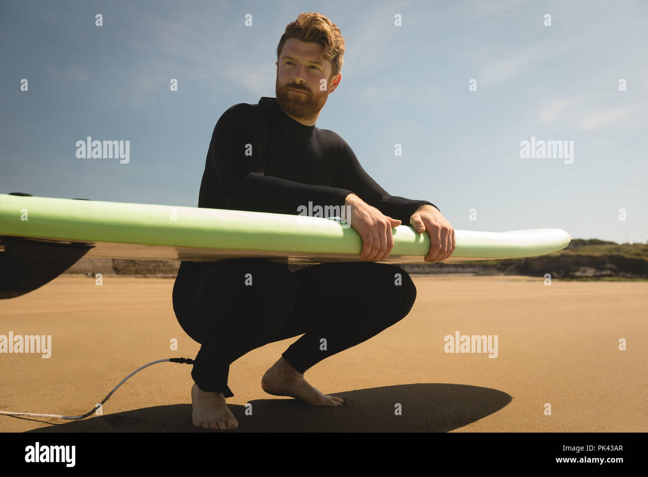 Surfer mit Surfbrett am Strand sitzen Stockfoto