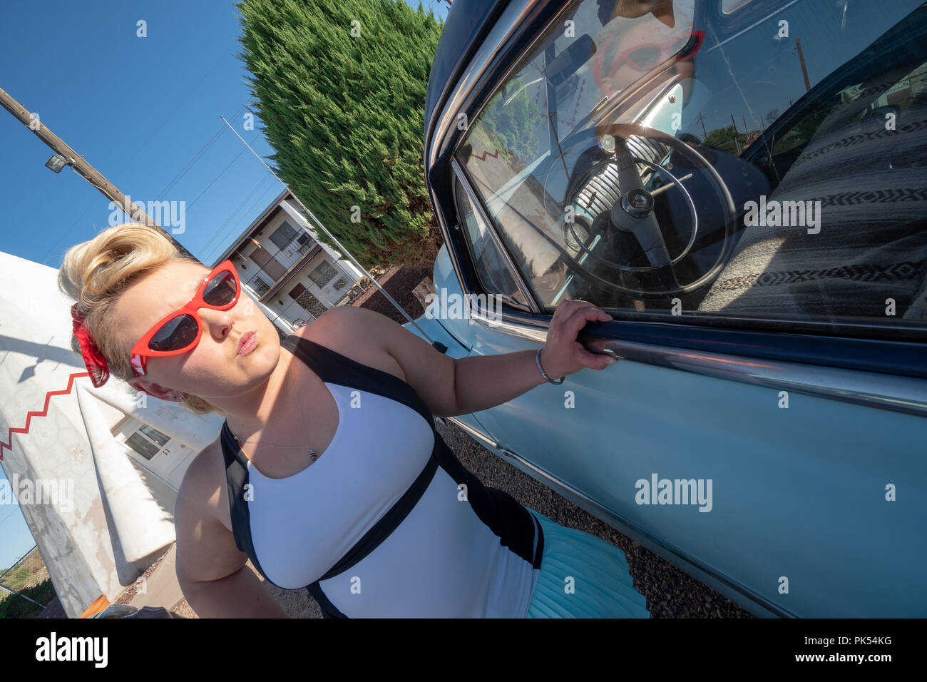 Blond erwachsenen Weibchen mit einem 1950er Jahrgang Pin up Frisur steht in der Nähe ein verlassenes Oldtimer, das Tragen von Cat eye Sonnenbrille Stockfoto