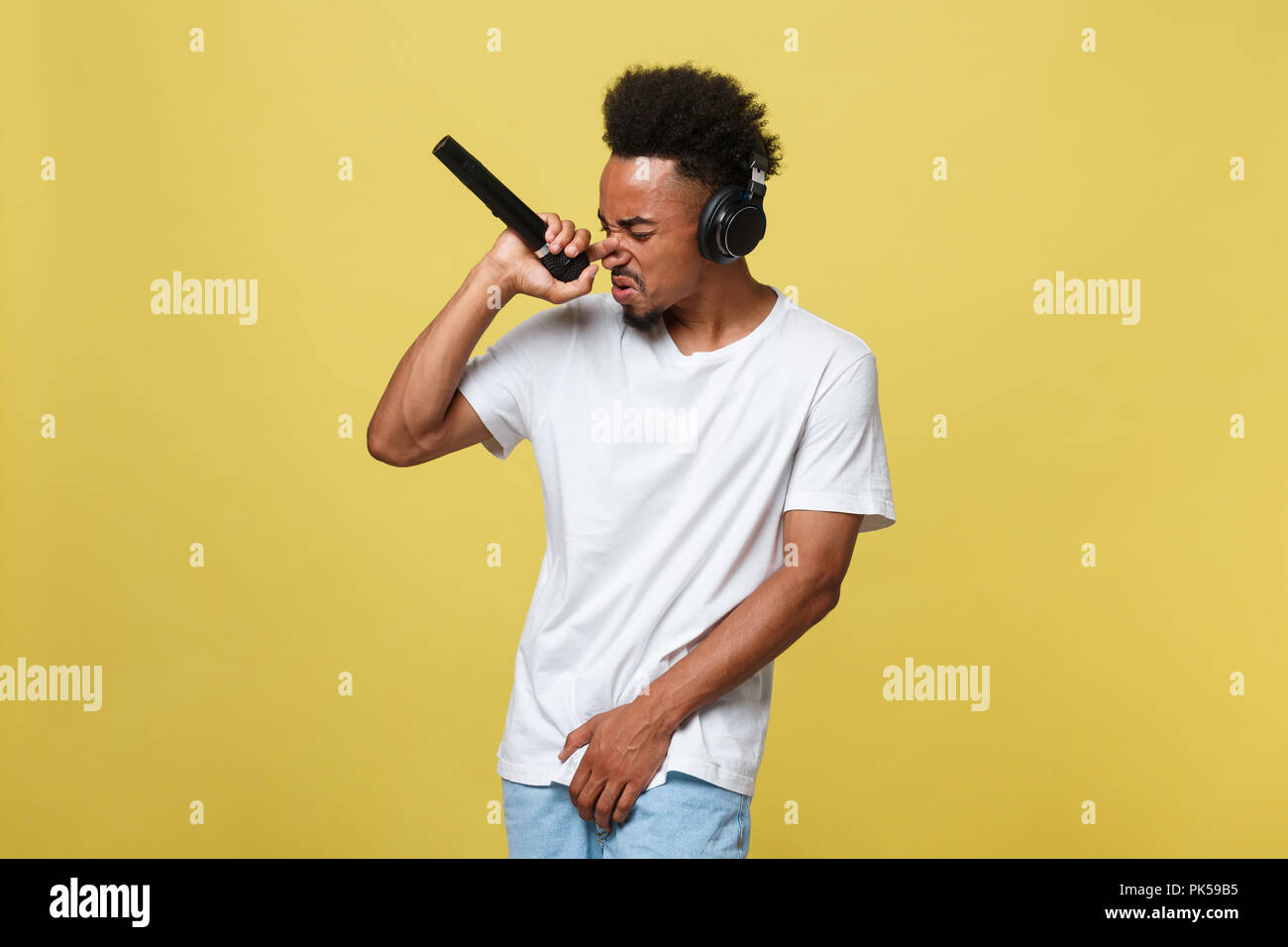 Attraktive junge dunkelhäutige Mann mit Afro Frisur im weißen T-Shirt, Gestikuliert mit der Hand und dem Mikrofon, Tanzen und Singen auf Party, Spaß haben. Stockfoto