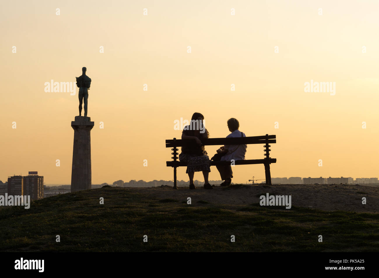 Belgrad Silhouetten in den Sonnenuntergang - zwei Frauen plaudern auf der Werkbank, mit Blick auf die Statue von Victor, Symbol der Stadt. Serbien. Stockfoto