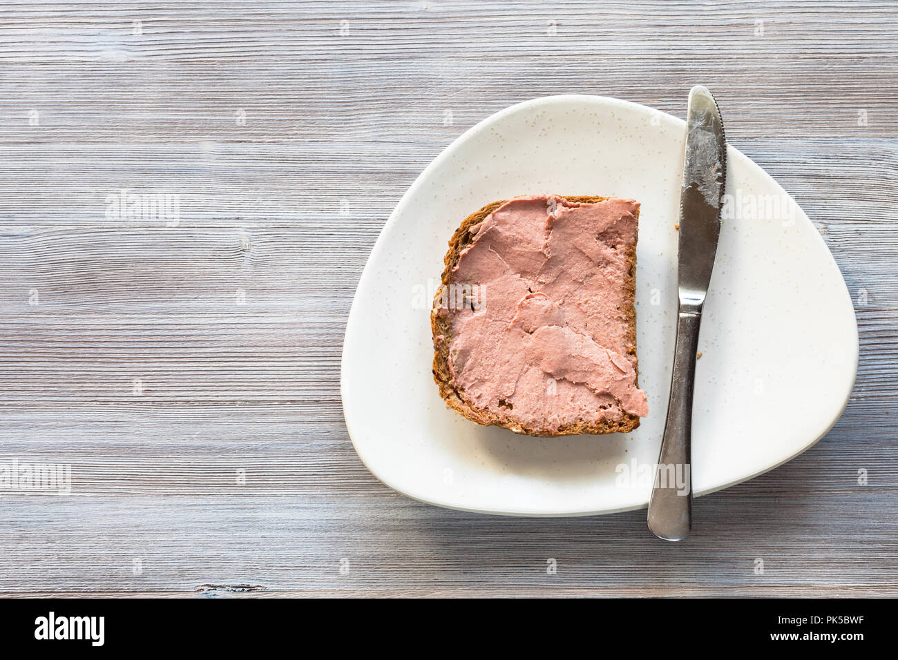 Blick von oben auf die Brot Sandwich mit Pastete und Stahl Messer auf weiße Platte auf grau Holzbrett mit leeren copyspace Stockfoto