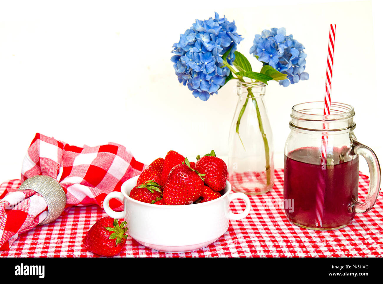 Patriotische, Rot, Weiß und Blau, Tisch mit Tischset, Schüssel mit Erdbeeren, Getränke im Glas mug und blaue Blumen in der Vase. Stockfoto