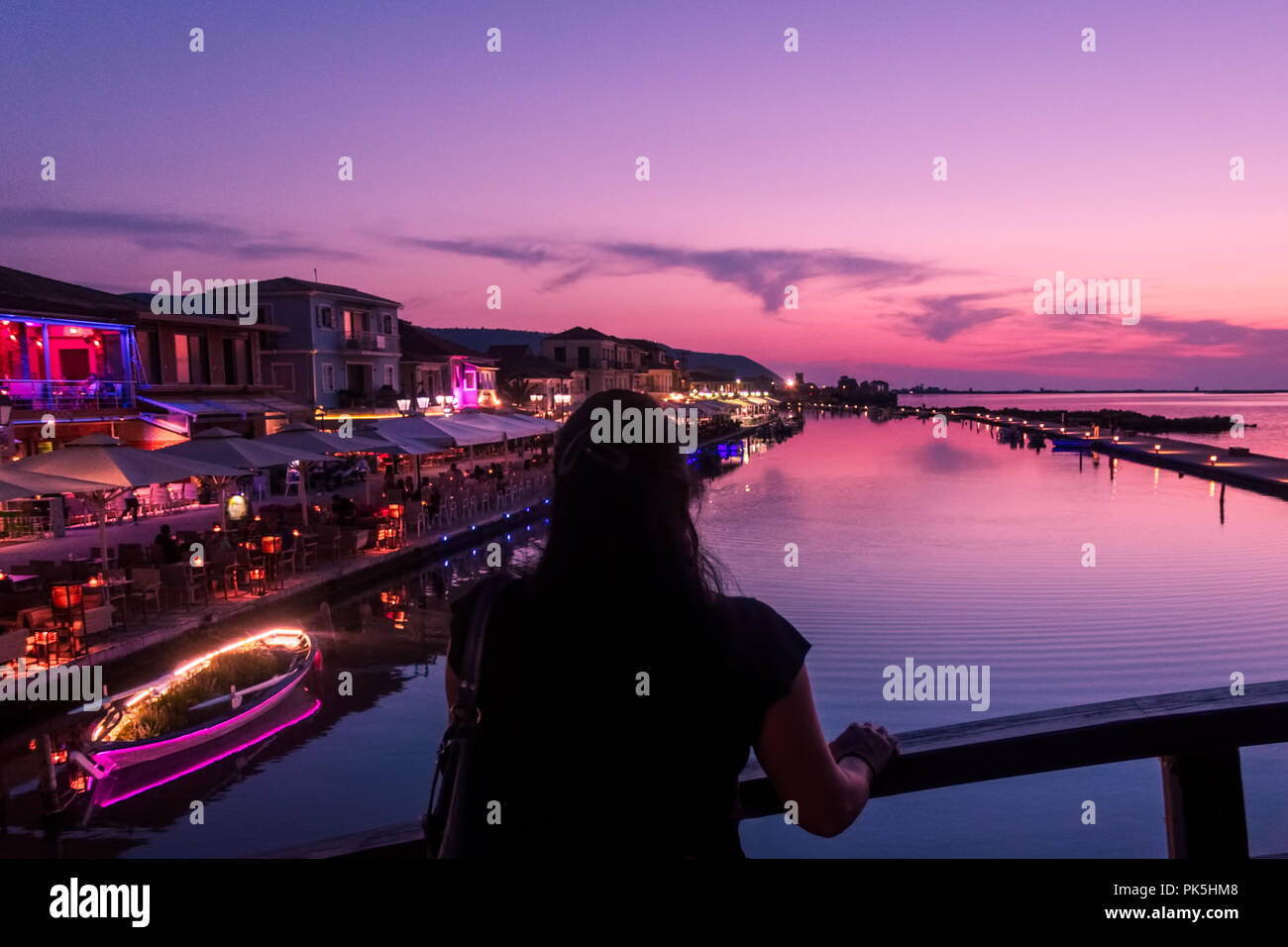 Frau mit dem Rücken zur Kamera, die den Sonnenuntergang auf der Marina-Brücke in Lefkada (Lefkas), Griechenland, beobachtet Stockfoto