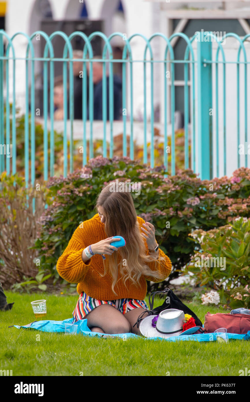 Ein Festival goer Entspannen im Festival Nummer 6 Spielen mit ihrem Haar und setzte sich auf ein Picknick Matte, Portmeirion, Wales Stockfoto
