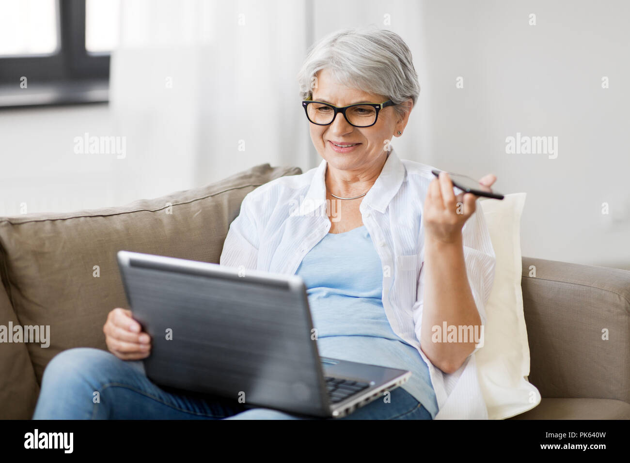 Alte Frau mit Laptop Datensätze Stimme von Smartphone Stockfoto