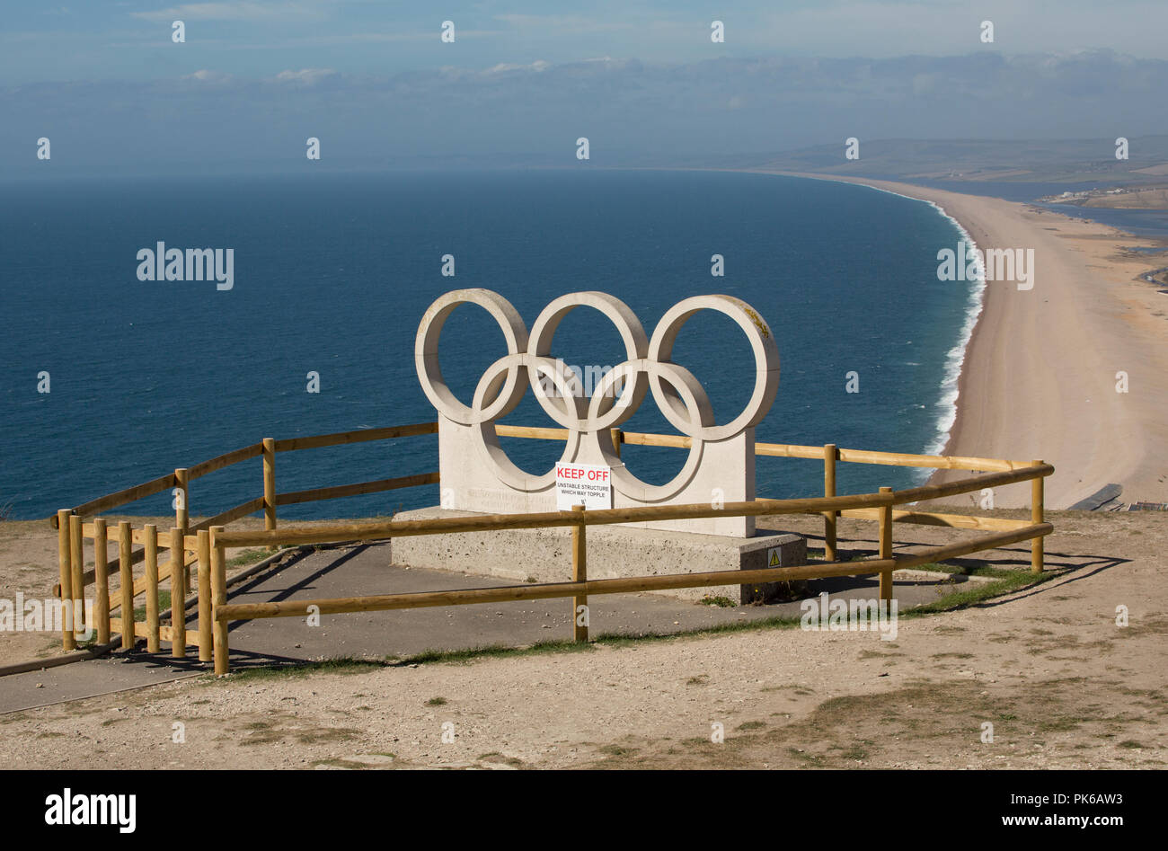 Eine steinerne Skulptur der Olympischen Ringe auf der Isle of Portland vor dem Hintergrund von Chesil Beach. Die Ringe wurden geschnitzt Weymouth und Por zu feiern. Stockfoto