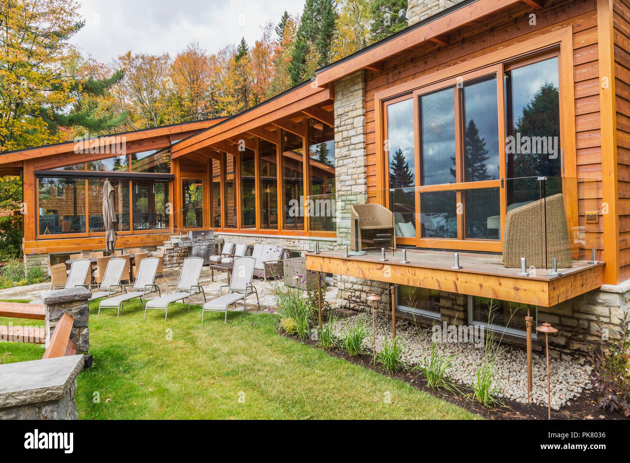 Ansicht der Rückseite des luxuriösen gefärbt Zedern-und Holz Home mit Panoramafenstern, Deck und Naturstein Terrasse im Herbst, Quebec Stockfoto