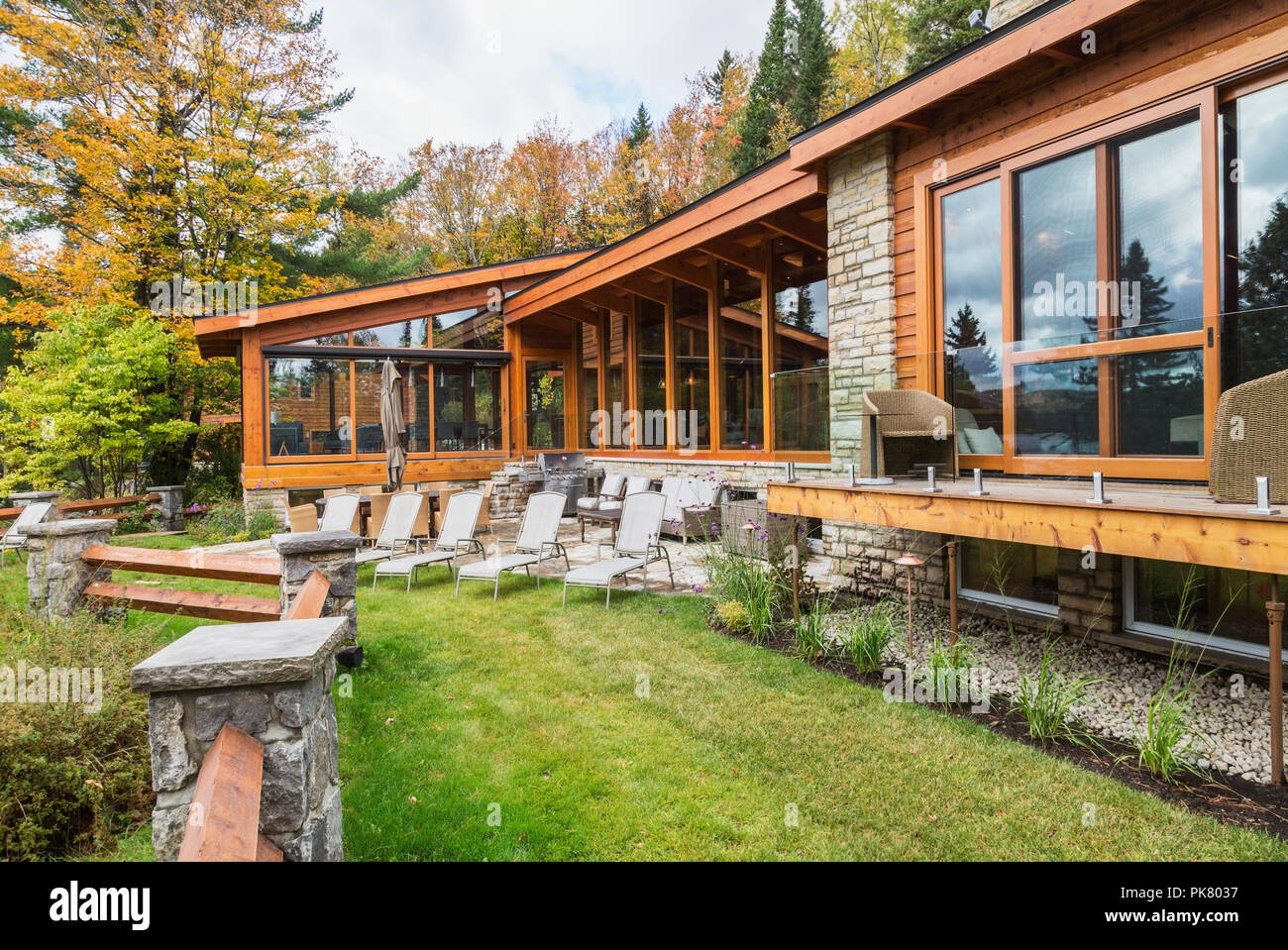 Ansicht der Rückseite des luxuriösen gefärbt Zedern-und Holz Home mit Panoramafenstern, Deck und Naturstein Terrasse im Herbst, Quebec Stockfoto