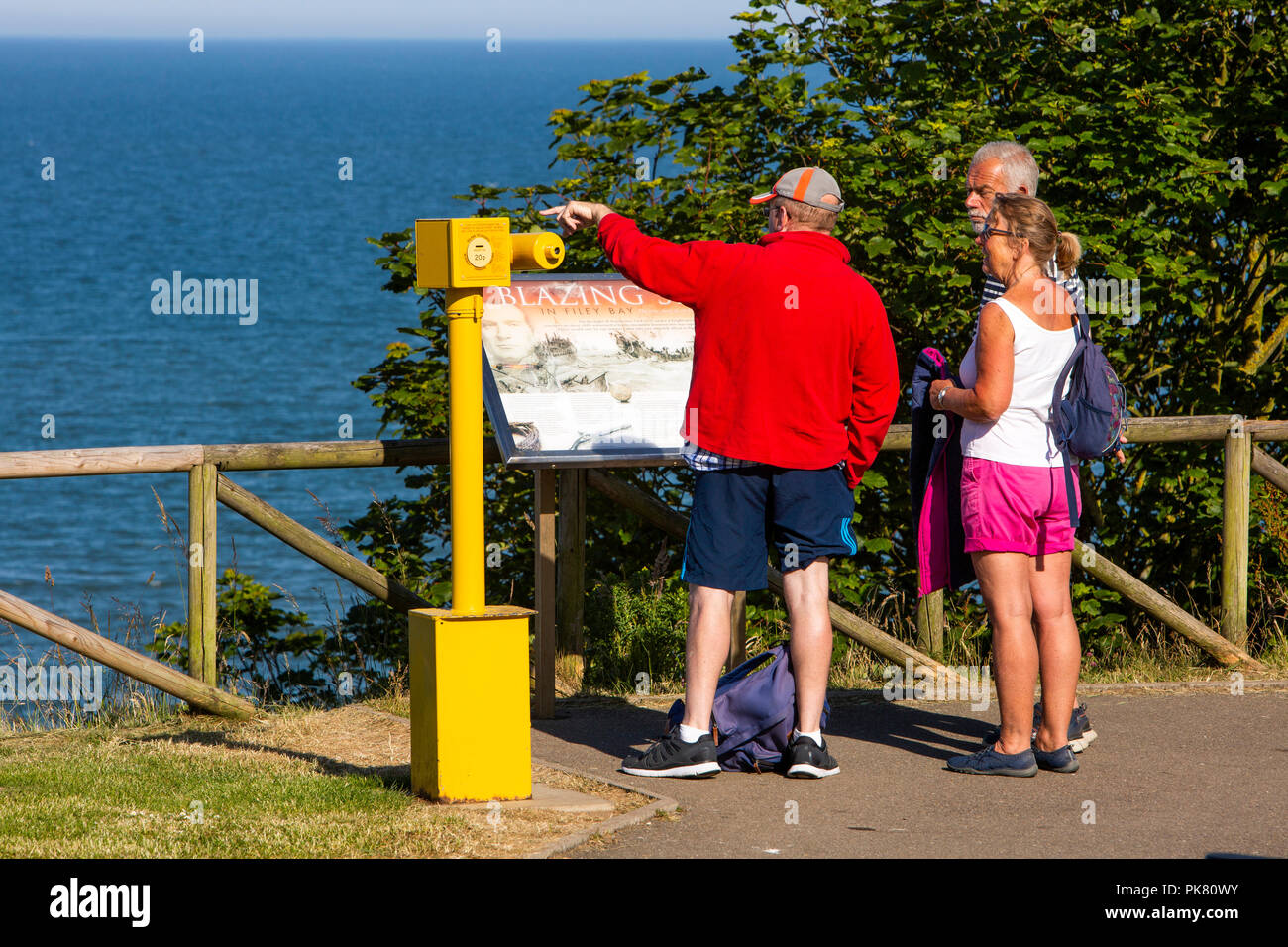 Vereinigtes Königreich, England, Yorkshire, Filey, Crescent Gardens, Besucher bei Münzeinwurf Teleskop über Filey Bay John Paul Jones an der Seeschlacht Information Board Stockfoto