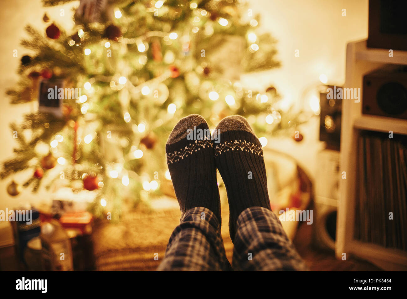 Festliche Socken auf alten hölzernen Stuhl auf dem Hintergrund der Goldenen schönen Christbaum mit Lichtern in festlichen Raum. Entspannen. gemütlichen Winterurlaub. warm Stockfoto