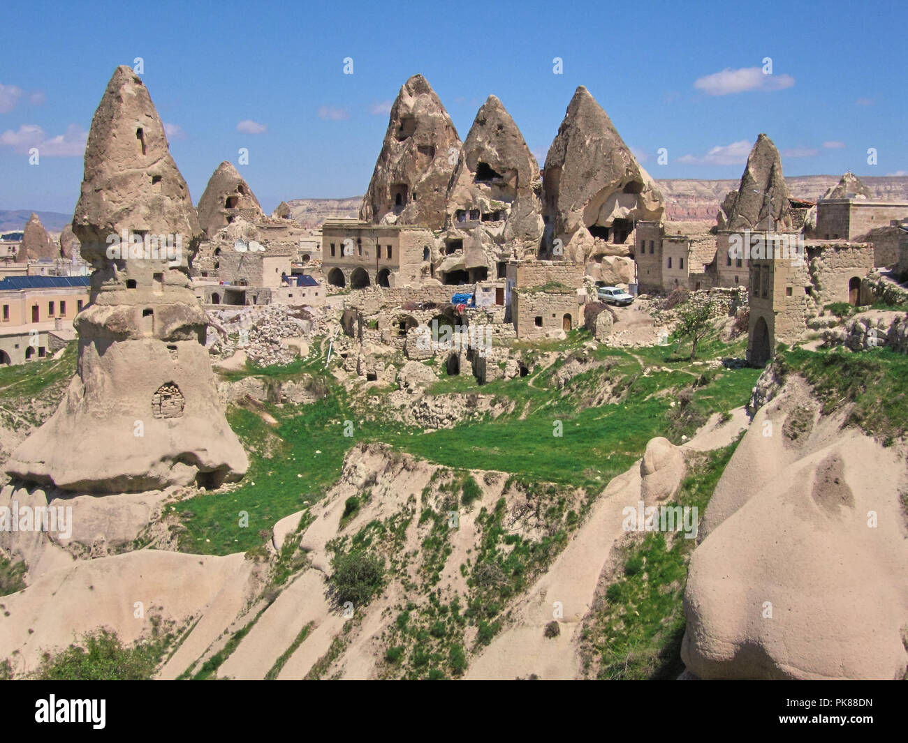 Höhlenwohnungen geschnitzt in Felsformationen mit grünem Gras und ein blauer Himmel in Göreme Stockfoto