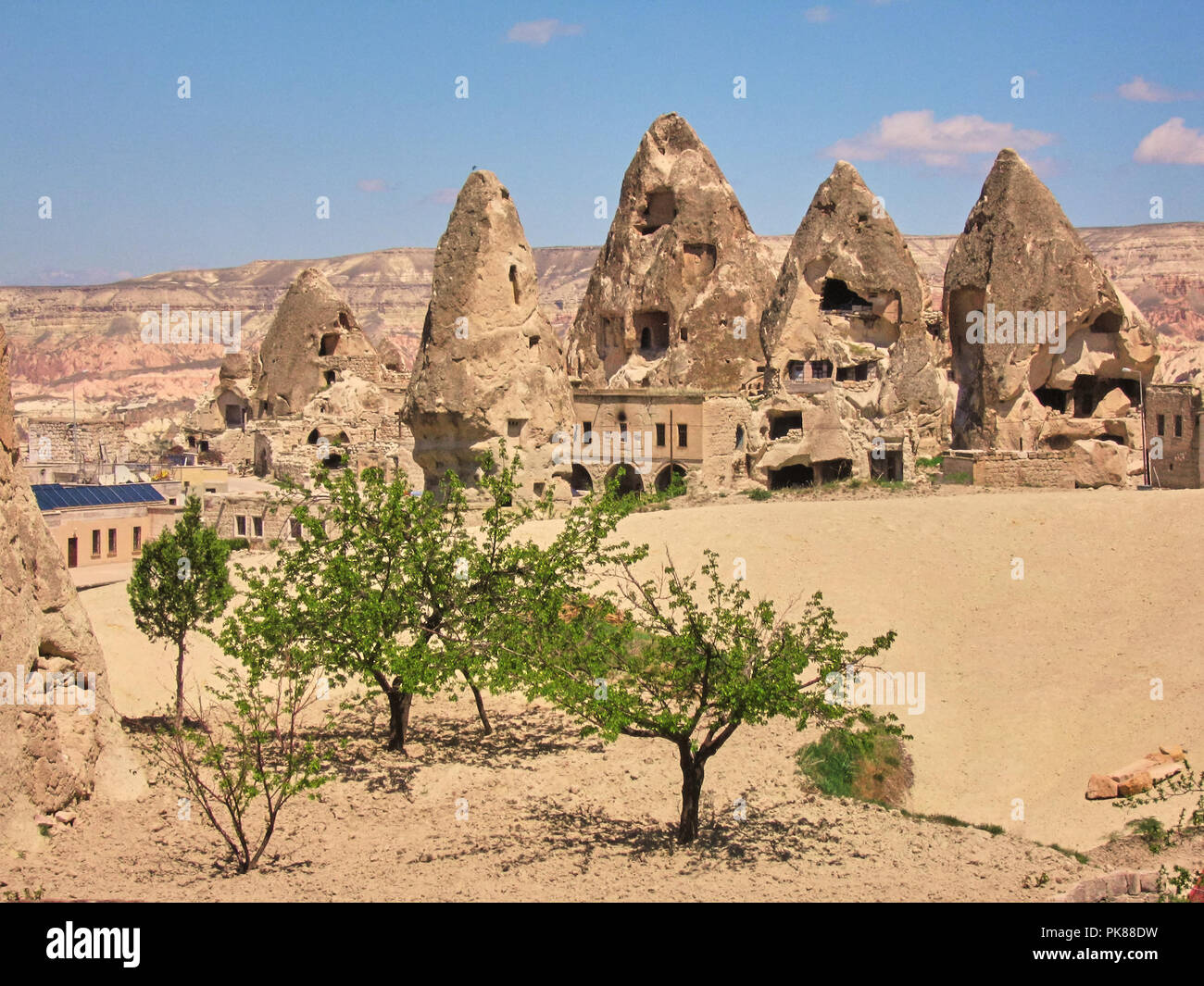 Höhlenwohnungen geschnitzt in Felsformationen mit grünem Gras und ein blauer Himmel in Göreme Stockfoto