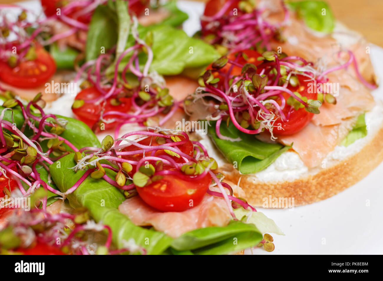 Hausgemachte kleine Sandwiches mit Sprossen, weißer Käse Salat, coctail Tomaten und Räucherlachs auf weiße Platte Stockfoto