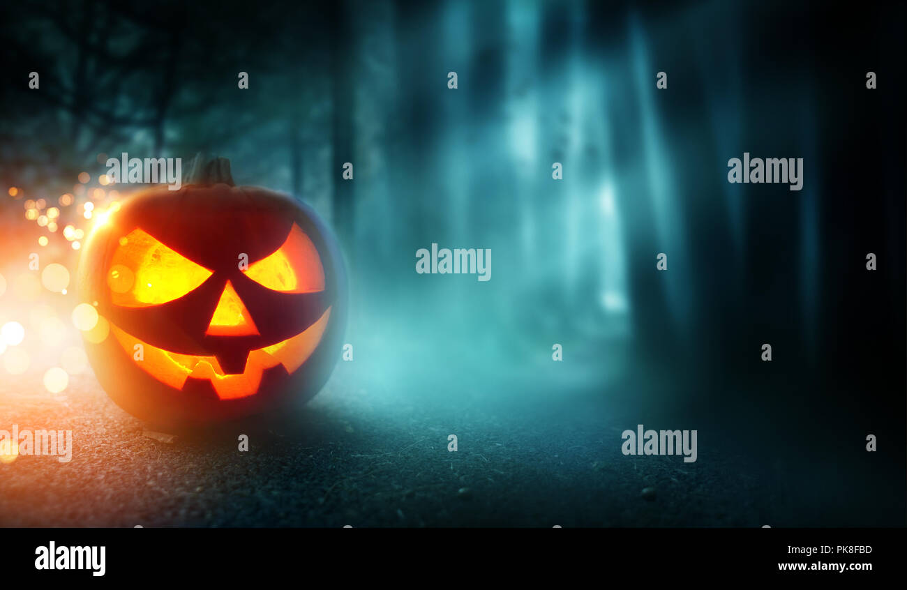 Ein gruseliges Halloween Kürbis Jack O'Lantern an einem nebligen, dunklen Abend mit einem nebligen Wald im Hintergrund grinsend. Stockfoto