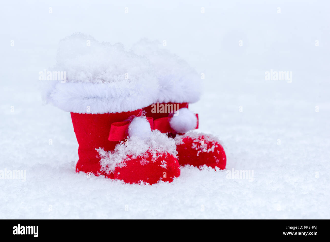 Kleine rote gefilzte Santa Claus Stiefel mit Fell Dekoration auf Schnee Weihnachten Hintergrund. Stockfoto