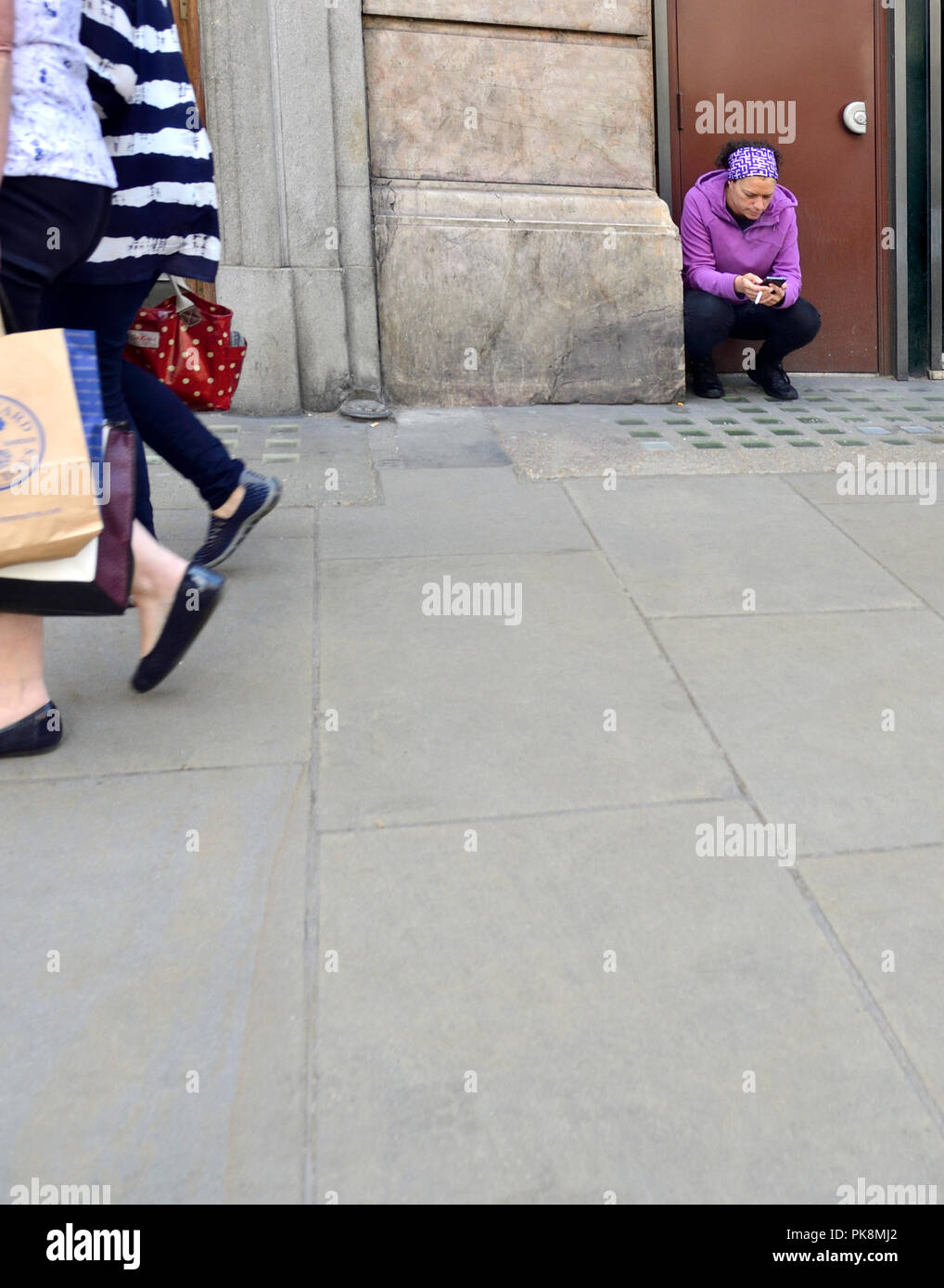 Frau kniete auf der Straße mit einer Zigarette und einem Mobiltelefon, London, England, UK. Stockfoto