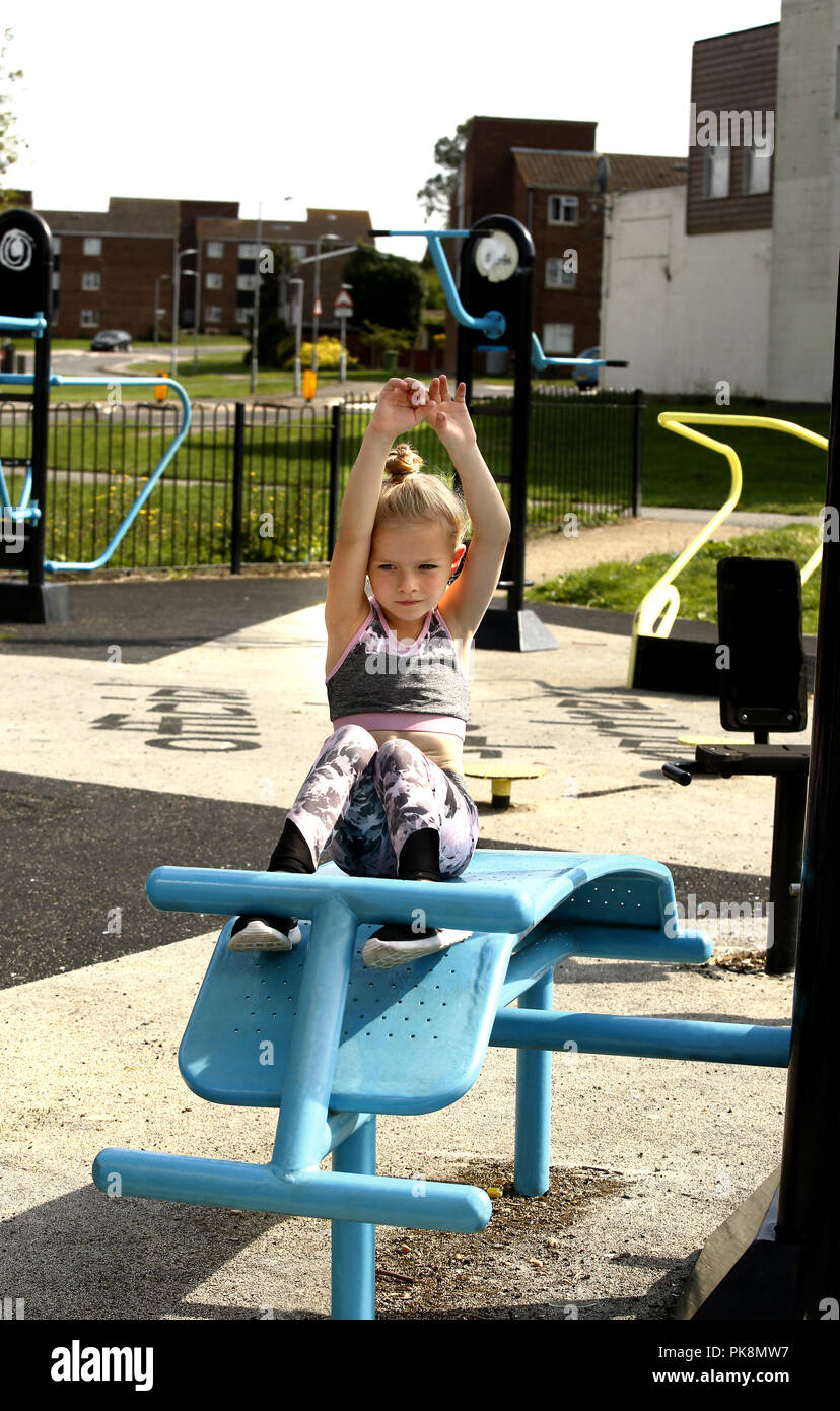 Ein sechs Jahre altes Mädchen macht das ups' auf freie Geräte in einer Fitness im Freien Bereich zu verwenden Stockfoto