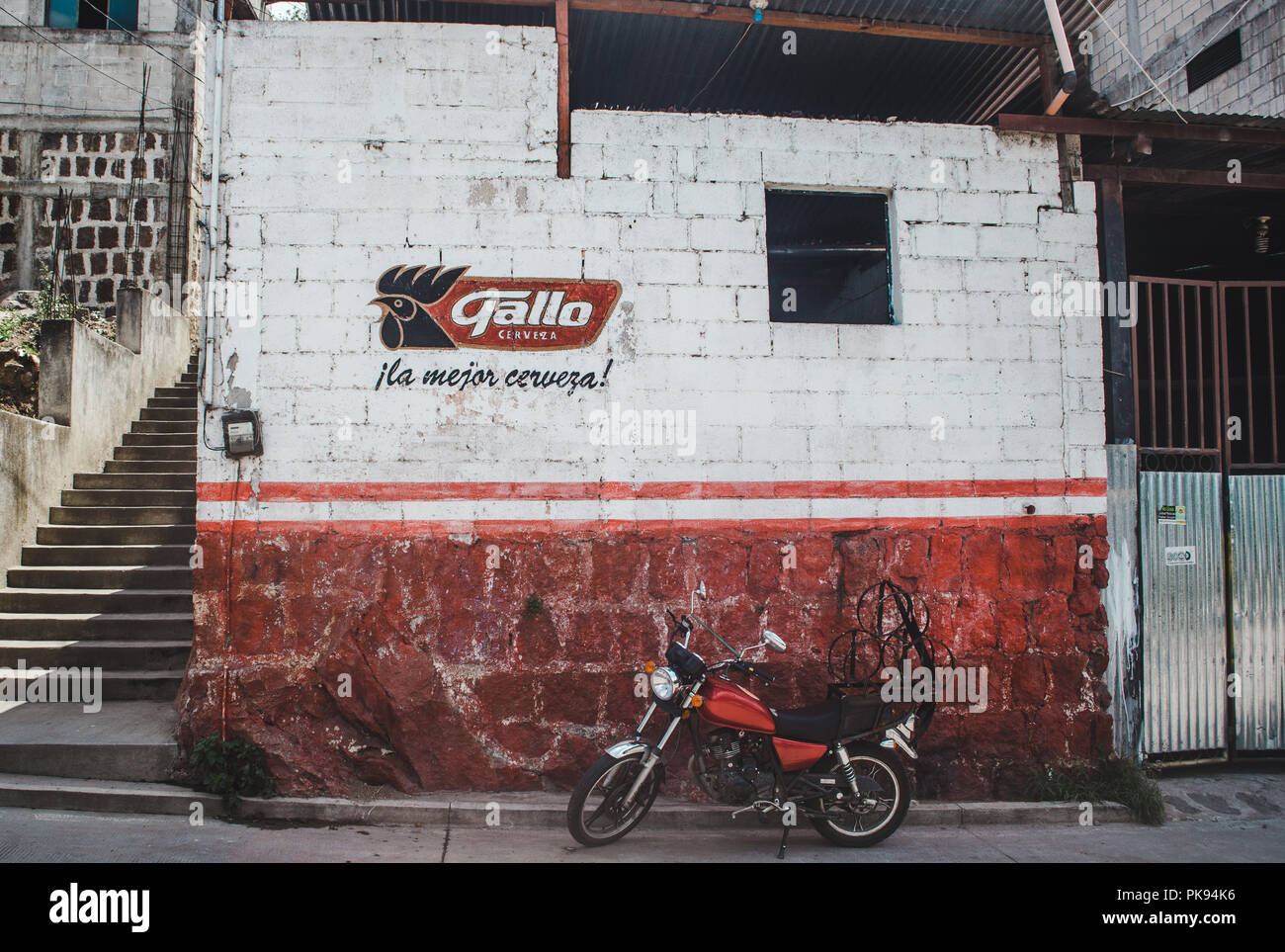 Rote Motorrad vor einer Bar mit Logo von Gallo, Guatemala nationalen Bier, spraypainted auf der Wand geparkt Stockfoto
