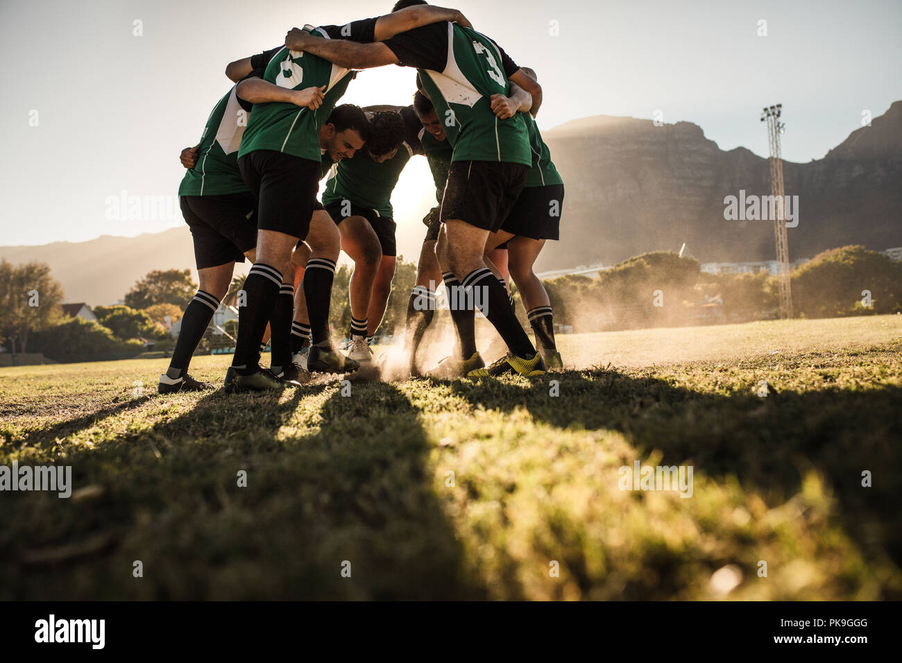 rugby-Spieler in einer Huddle, die ihre Füße auf dem Gras reiben. rugby-Team zeigt Aggression nach dem Sieg. Stockfoto