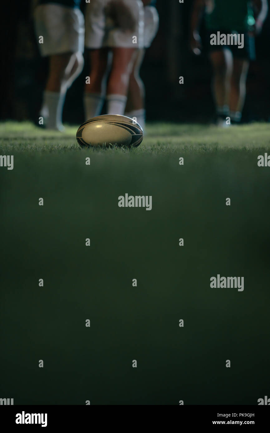 rugbyball auf Rasen mit Teams im Hintergrund. Ball auf dem Boden mit Spielern auf der Rückseite während des Rugby-Spiels. Stockfoto