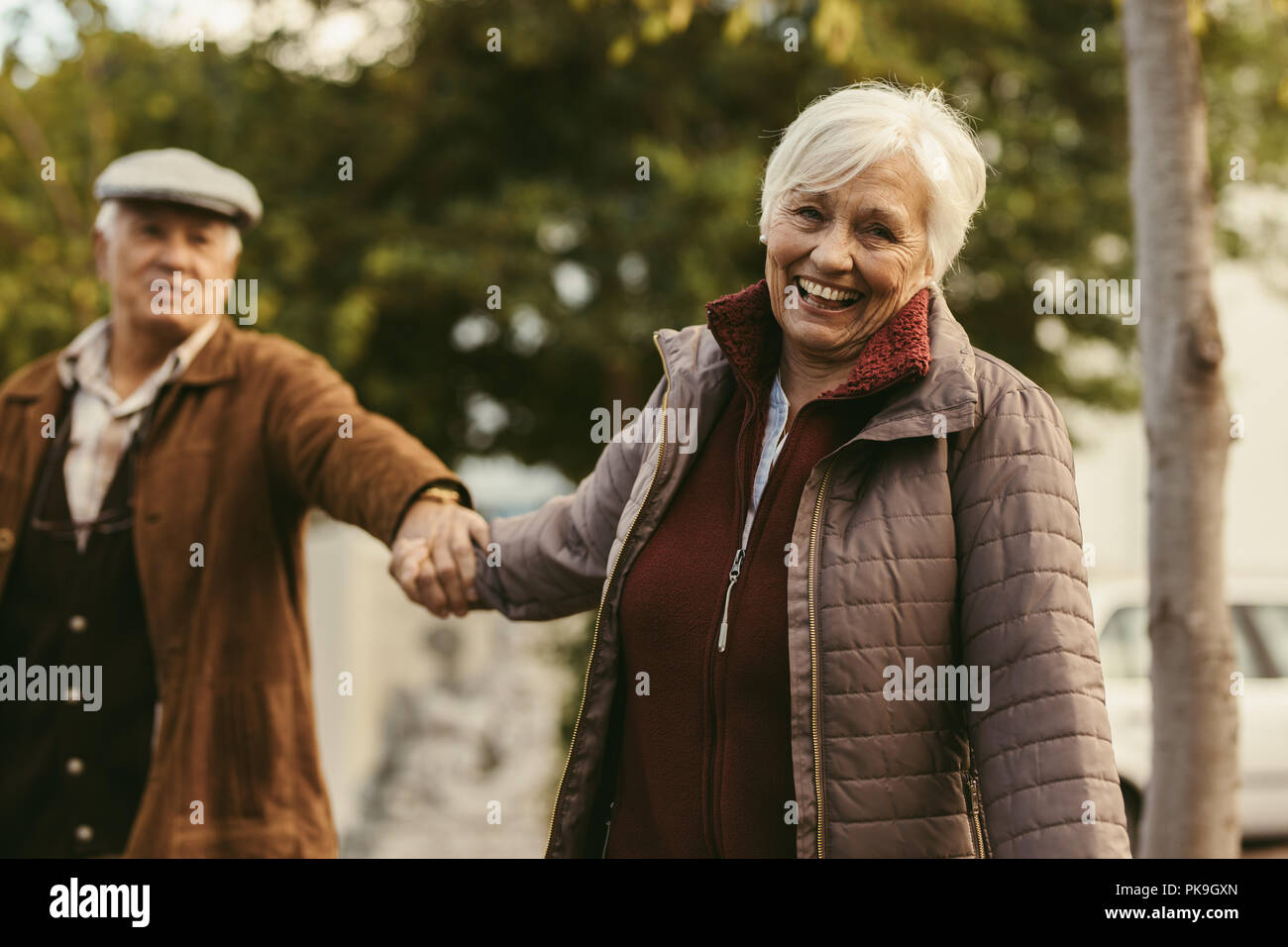 Lächelnd senior woman holding hand Ihrer Partner und Wandern in der freien Natur. Gerne älteres Paar im Freien an einem Wintertag. Stockfoto