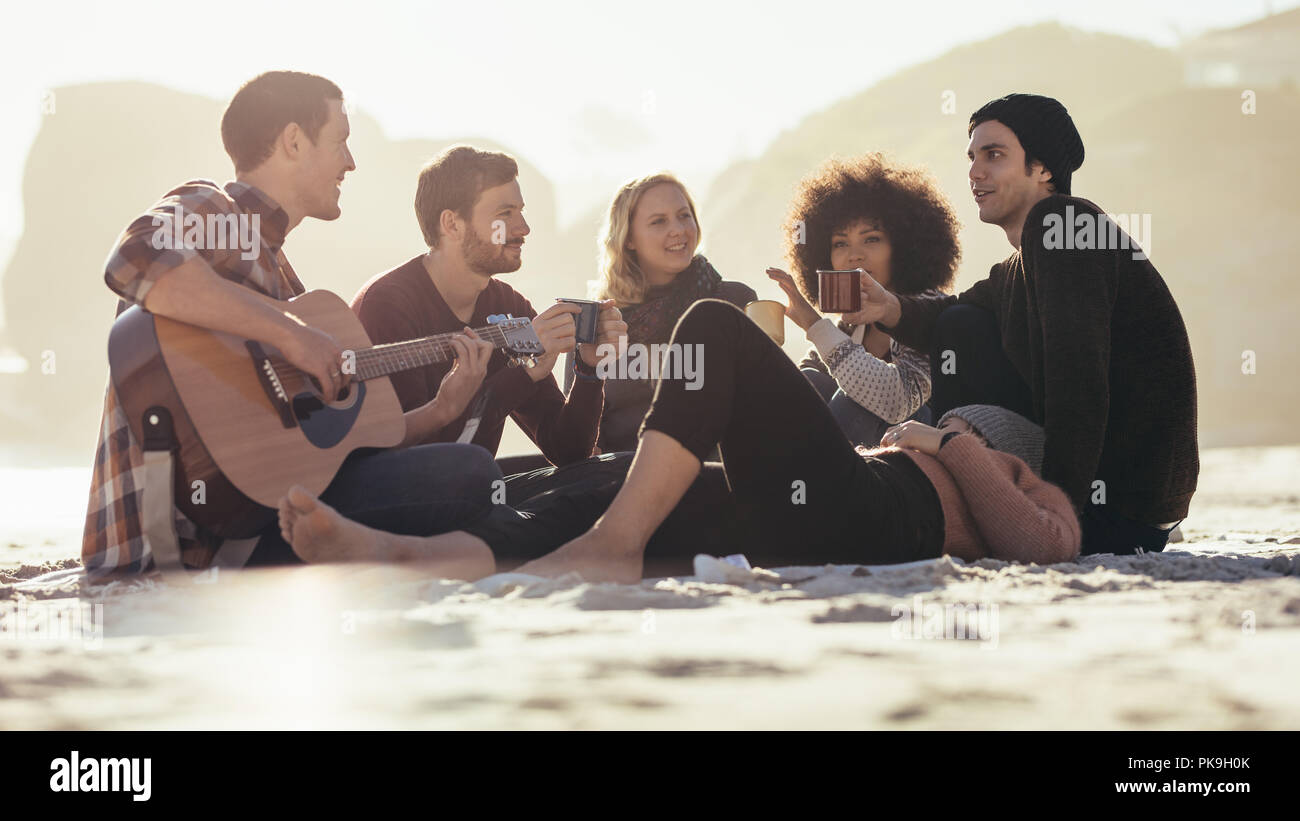 Junger Mann mit Gitarre für Freunde am Strand. Eine Gruppe von Freunden, die Party am Meer. Stockfoto