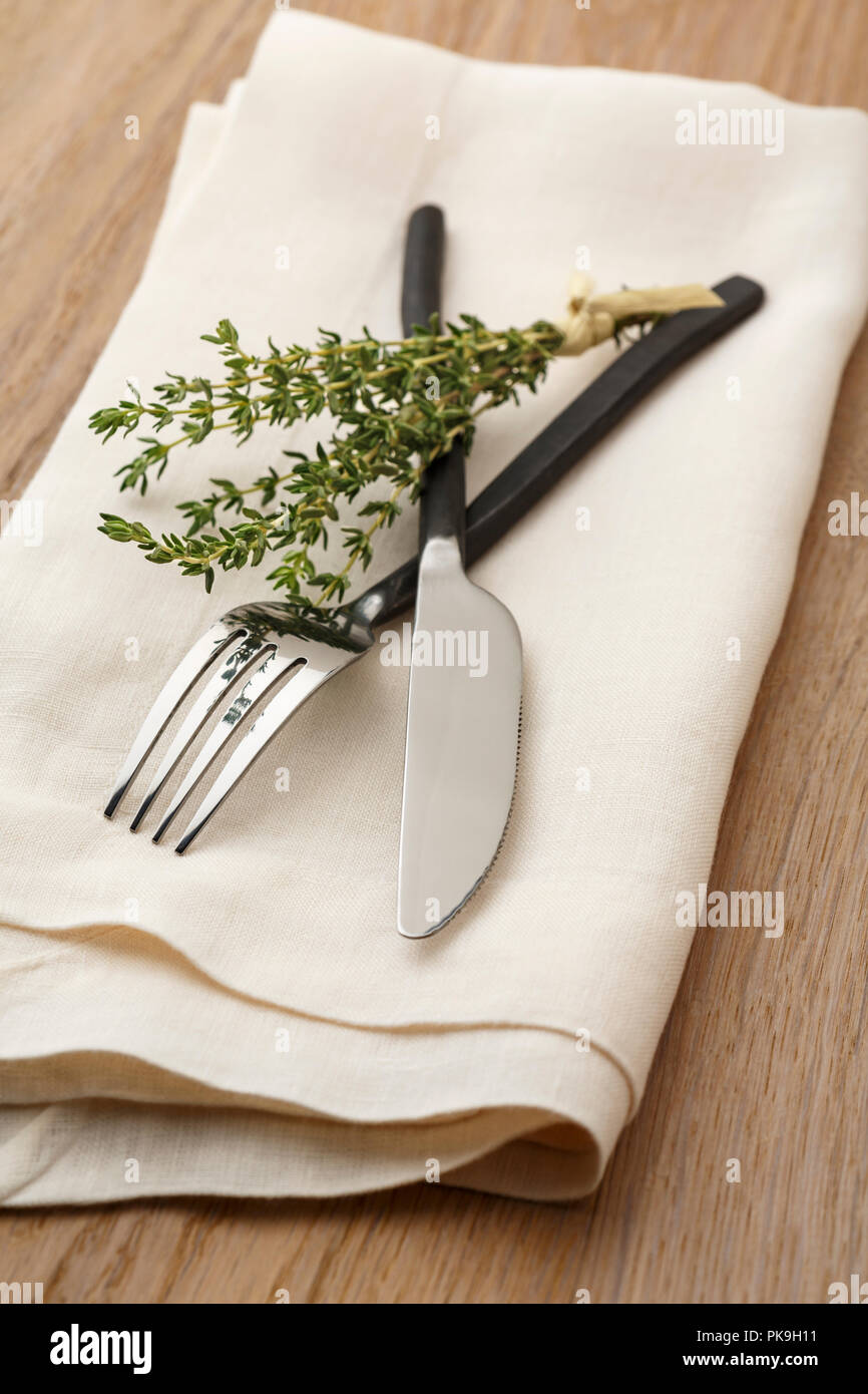 Casual handwerklichen Esstisch Platz Einstellung mit Messer und Gabel Besteck, Serviette und mit einem weißen Tuch einen Zweig frischen Bio Thymian Kräuter auf Holz Tisch Stockfoto