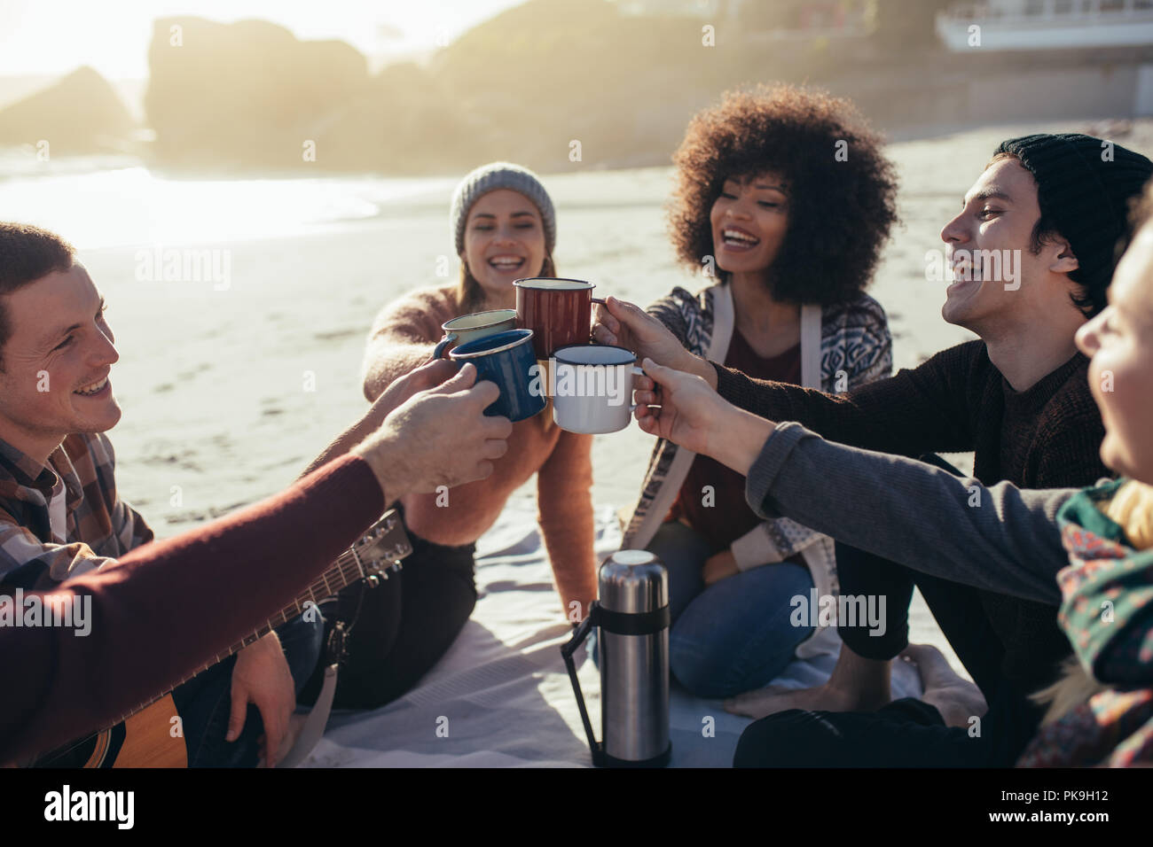 Gruppe von multi-ethnischen Jugendliche toasten Kaffeetassen am Strand. Eine Gruppe von Freunden die Zeit zusammen am Strand/in. Stockfoto