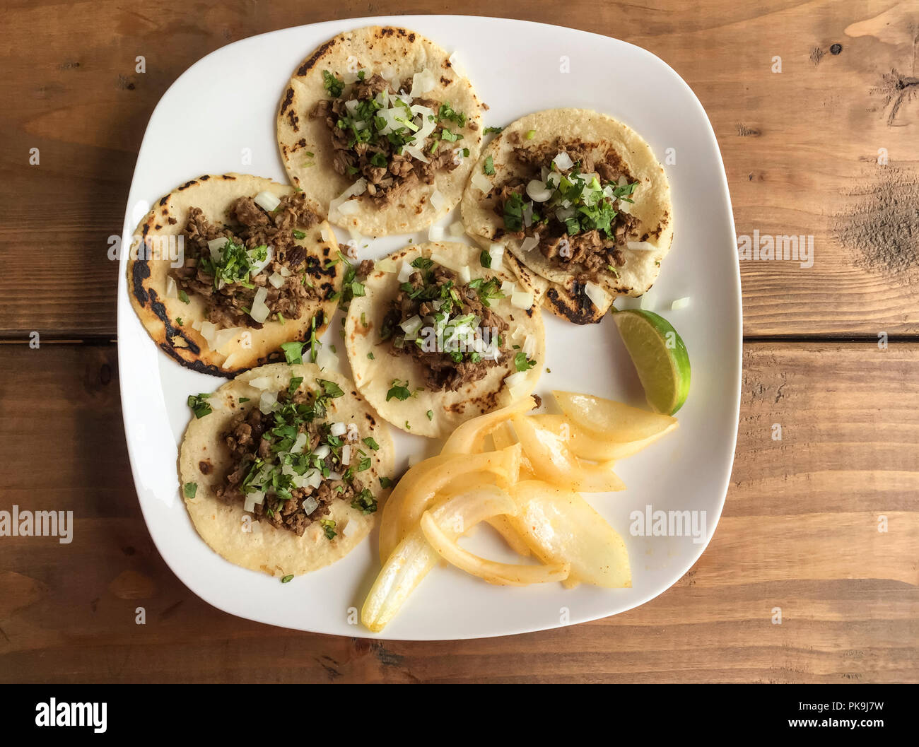 Traditionelle mexikanische Lebensmittel gegrilltes Rindfleisch fajitas Tacos auf weißer Keramik Platte mit Maistortillas, Zwiebeln, Koriander und Limette garnieren auf Holz Tisch Stockfoto