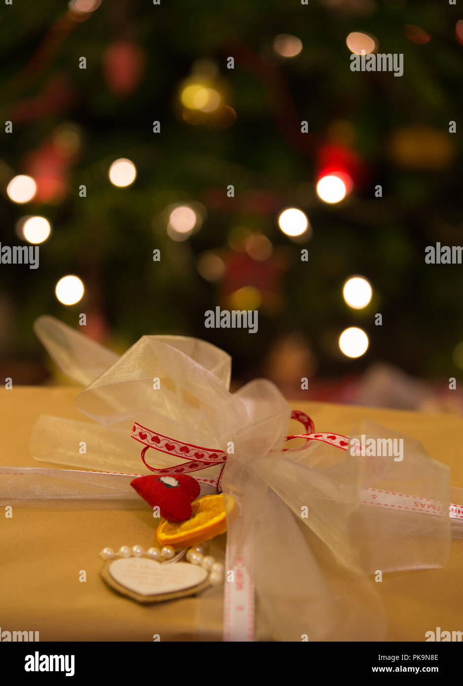 Wickelte Weihnachtsgeschenk, unscharf Weihnachtsbaum mit Lichterkette im Hintergrund Stockfoto