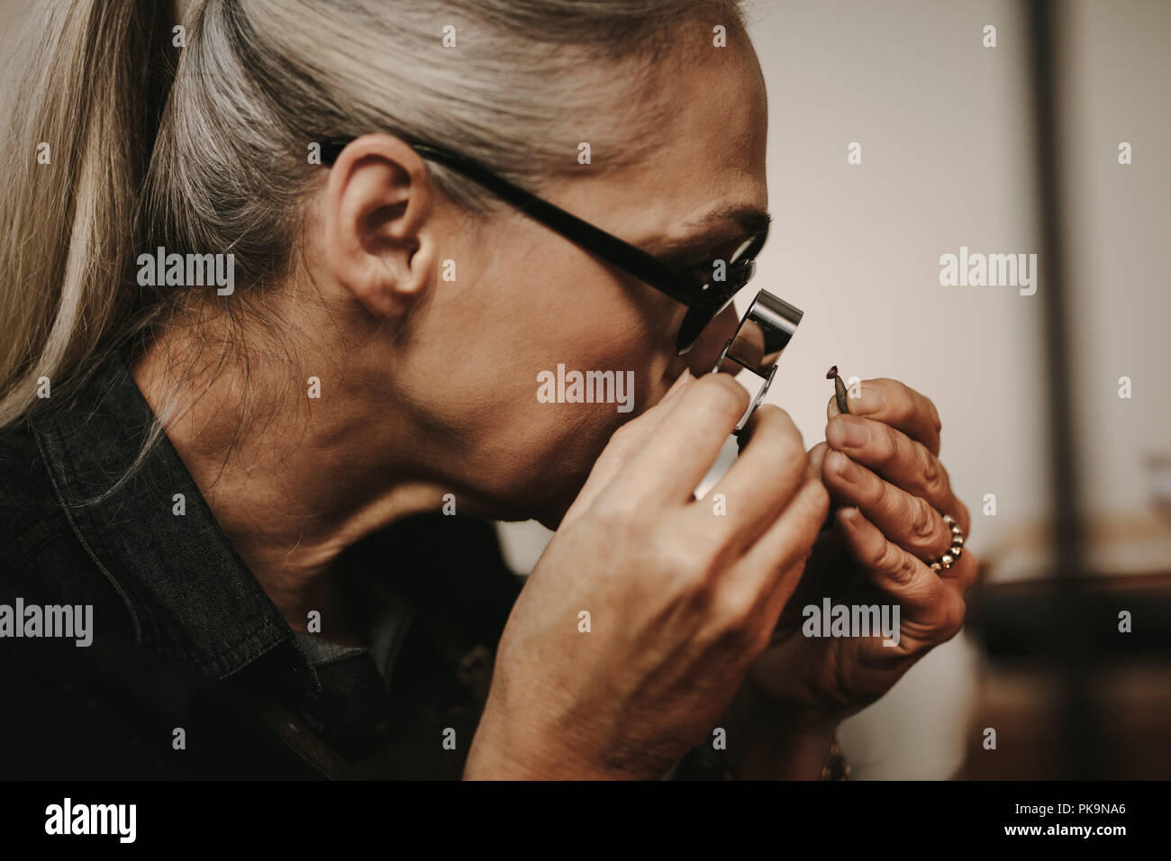 Nahaufnahme von Frau Juwelier diamant Prüfung Lupen-funktion Werkstattarbeit. close-up Senior weiblichen Juwelier bei Diamond durch Lupe Lupe suchen. Stockfoto
