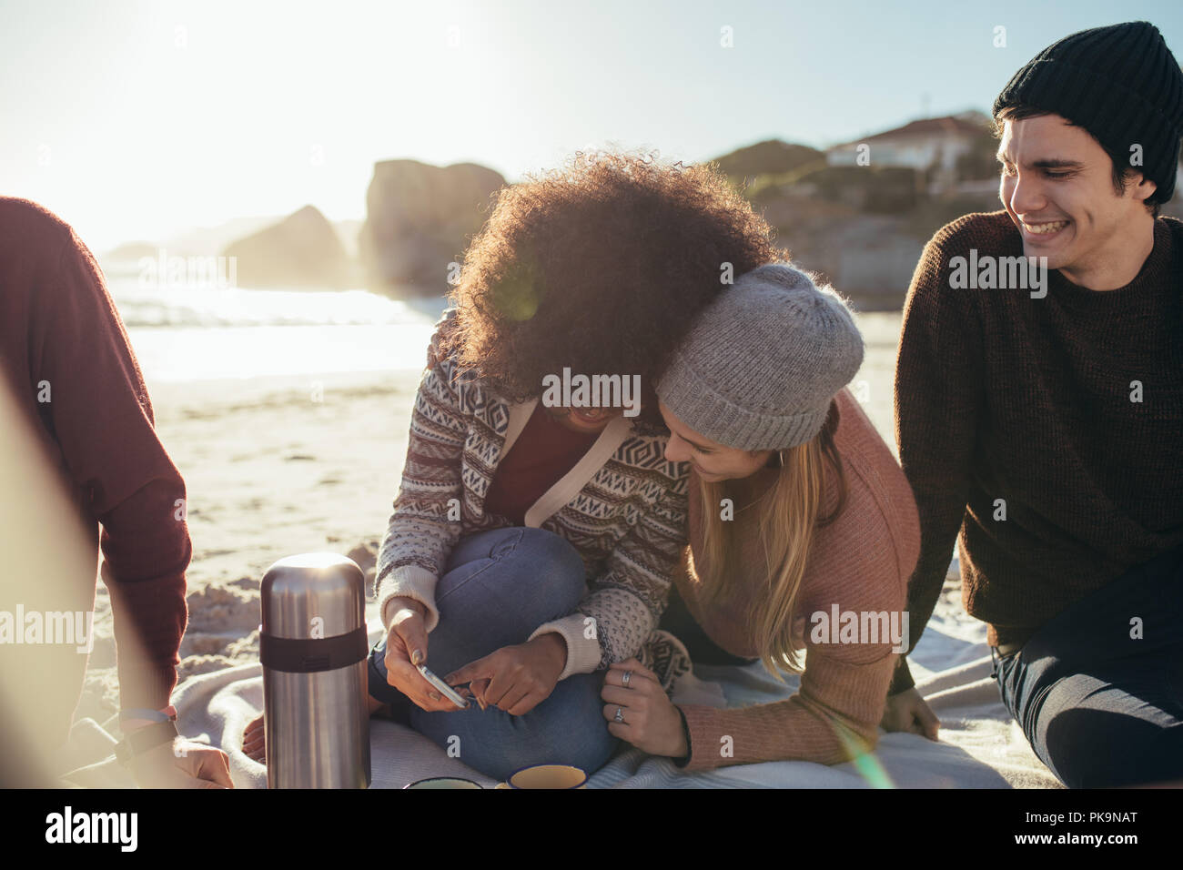 Zwei junge Frau sitzt auf den Strand etwas lustig auf Handy und lächelnd mit einem Freunde sitzen. Gruppe von Jugendlichen auf entspannende Stockfoto