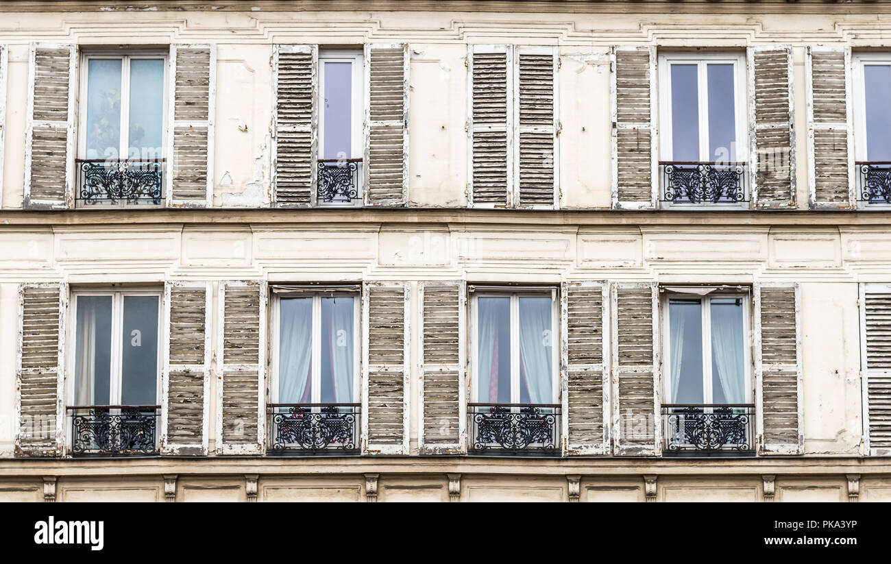 Holz Fensterläden mit abblätternder Farbe Flanke windows mit schwarzen schmiedeeisernen Geländer auf ein Gebäude in Paris, Frankreich. Stockfoto