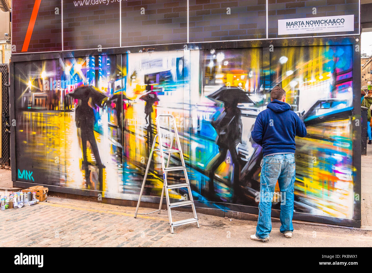 Ein Graffiti Künstler erstellen einer bunten regnerischen Nacht Zeit Straßenszene in Spitalfields, London, England, Großbritannien Stockfoto