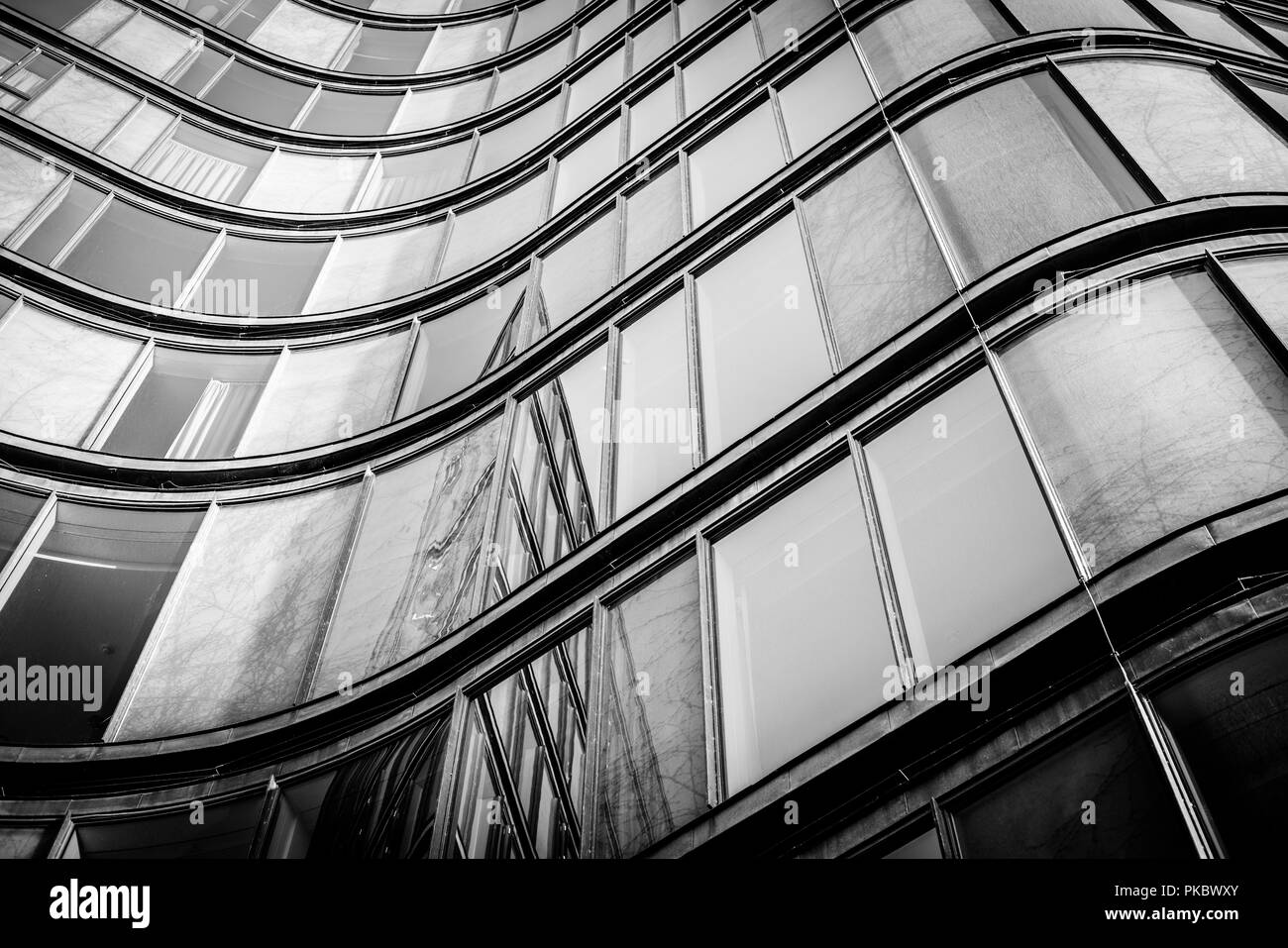 Geschwungene Gebäude mit glänzenden Fenstern mit Reflexionen in schwarzen und weißen Ton Stockfoto