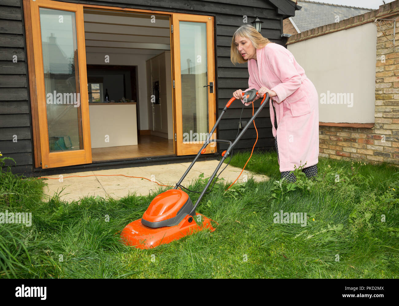Frau mähen Rasen einen Morgenmantel außerhalb tragen Stockfoto