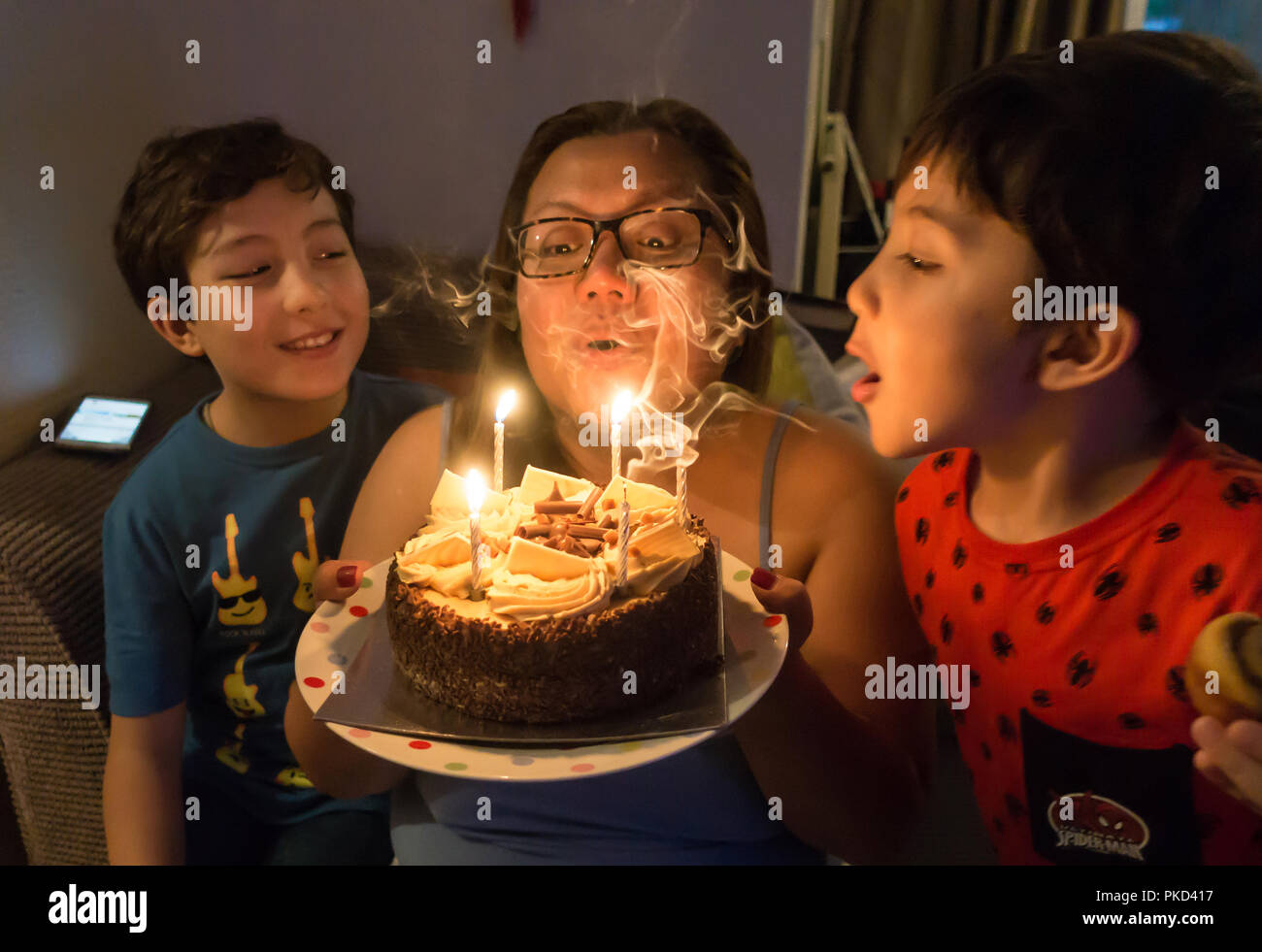 Eine Frau wird von ihrer Familie in das Ausblasen der Kerzen auf ihre Schokolade Kuchen geholfen. Stockfoto