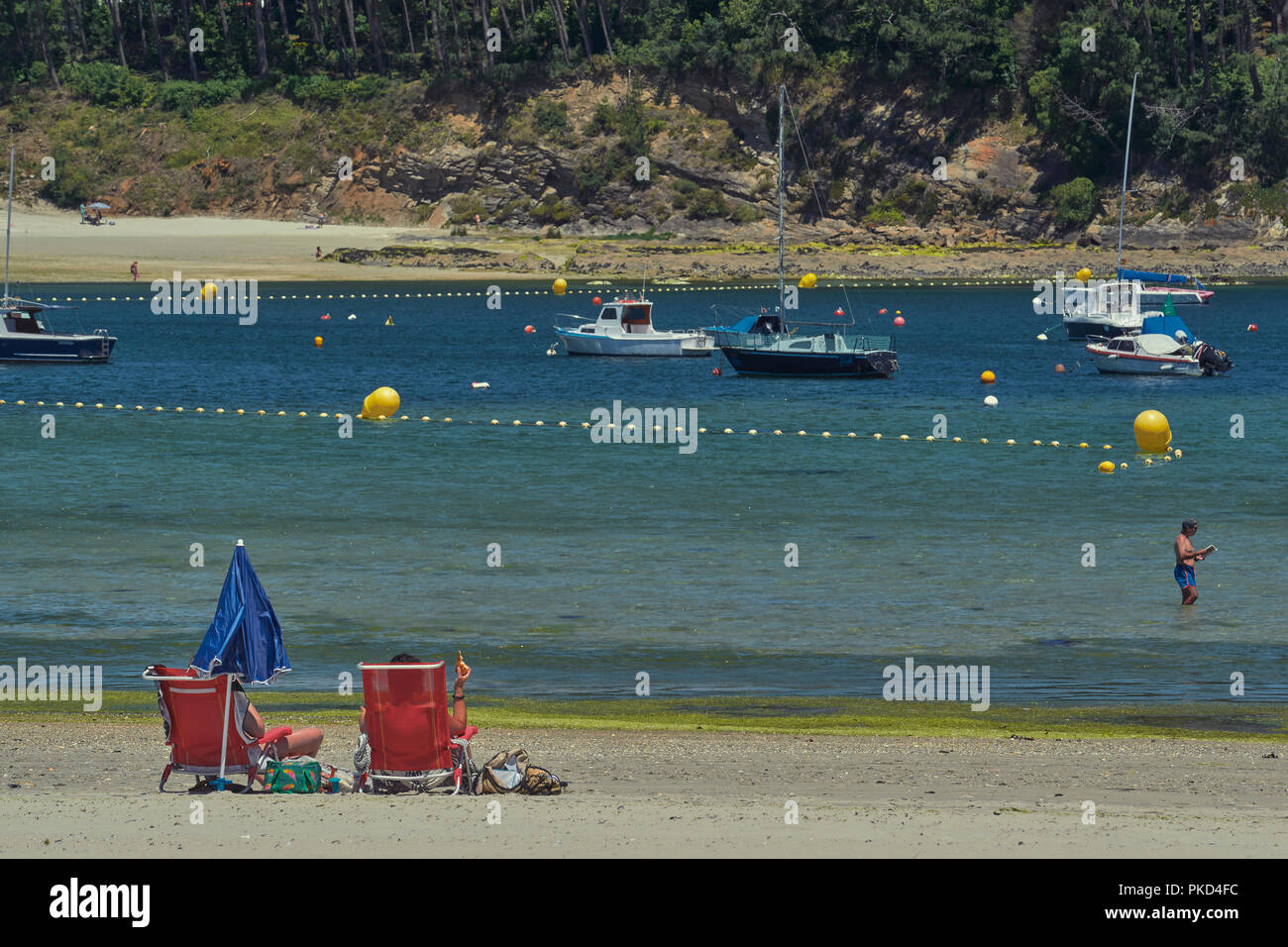 Zwei Touristen sitzen in Hängematten mit geschlossenen Schirm am Strand von Portonovo, Pontevedra, Galizien, Spanien, Europa Stockfoto
