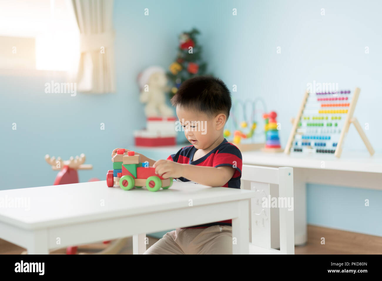 Adorable asiatischen Kleinkind Baby Junge sitzt auf einem Stuhl und Spielen mit Farbe Holz- zug Spielzeug zu Hause. Stockfoto